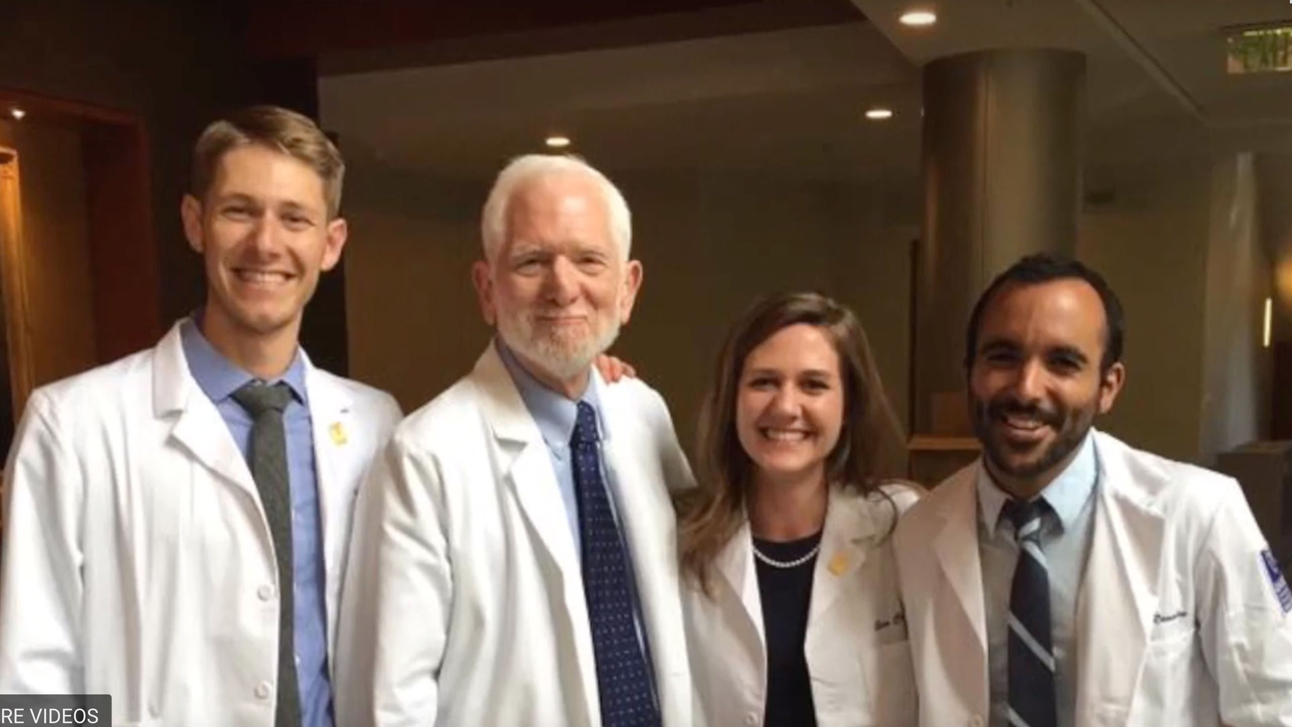Two medical students in white coats with doctors and professors.