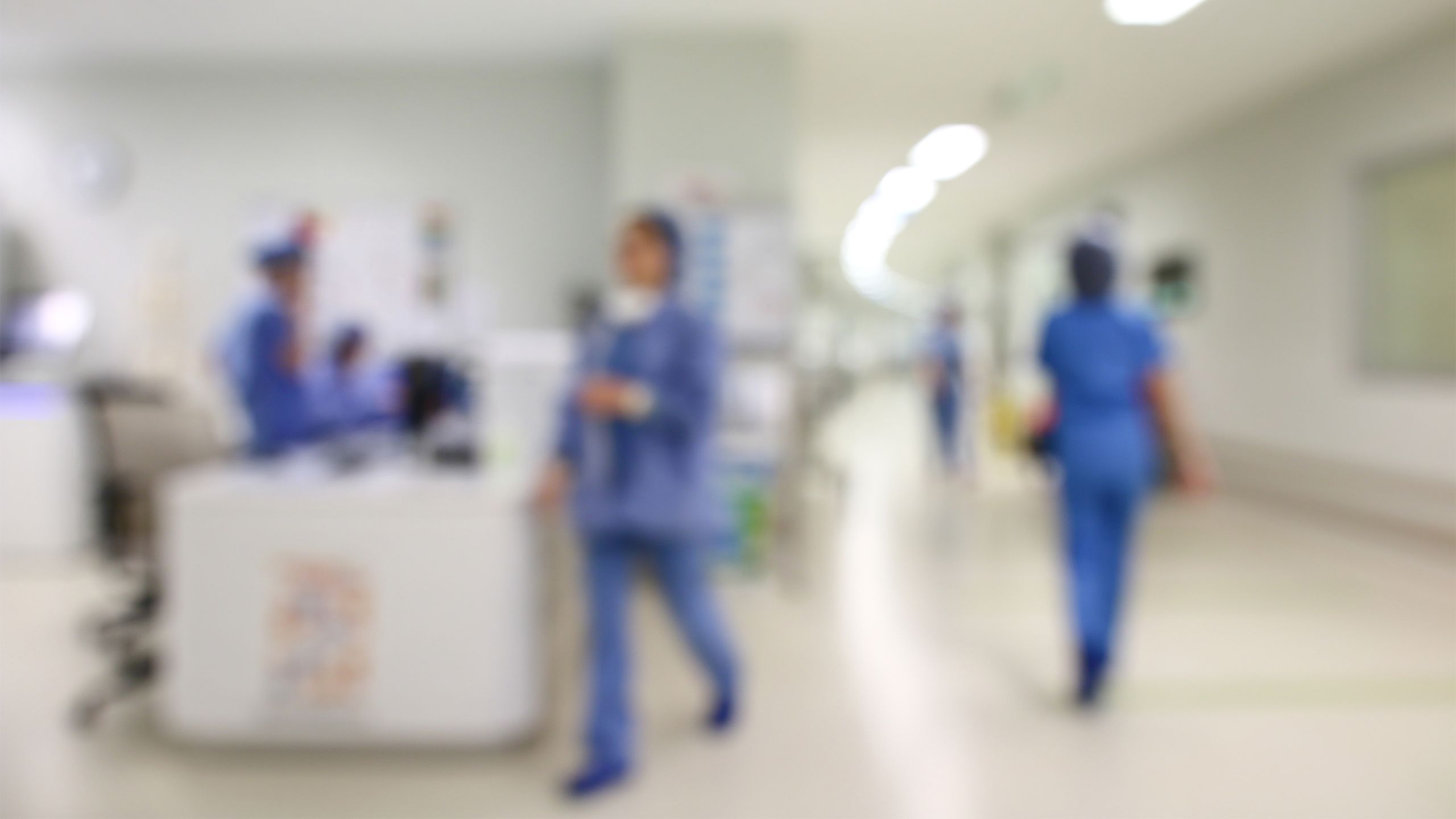 A blurred image shows nurses and other hospital staff walking