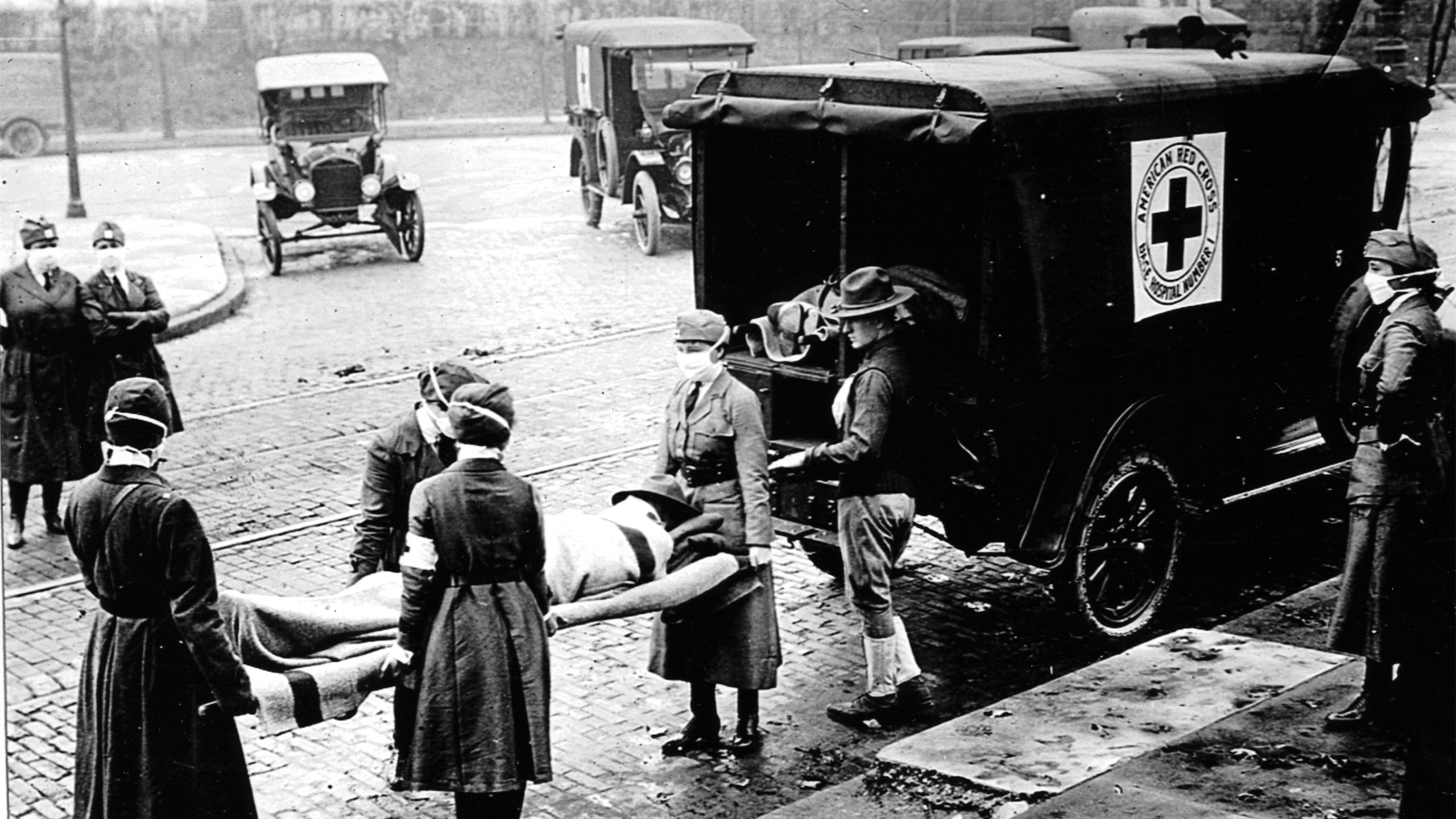 A historical image from 1918 shows a patient on a stretcher being placed in a Red Cross ambulance
