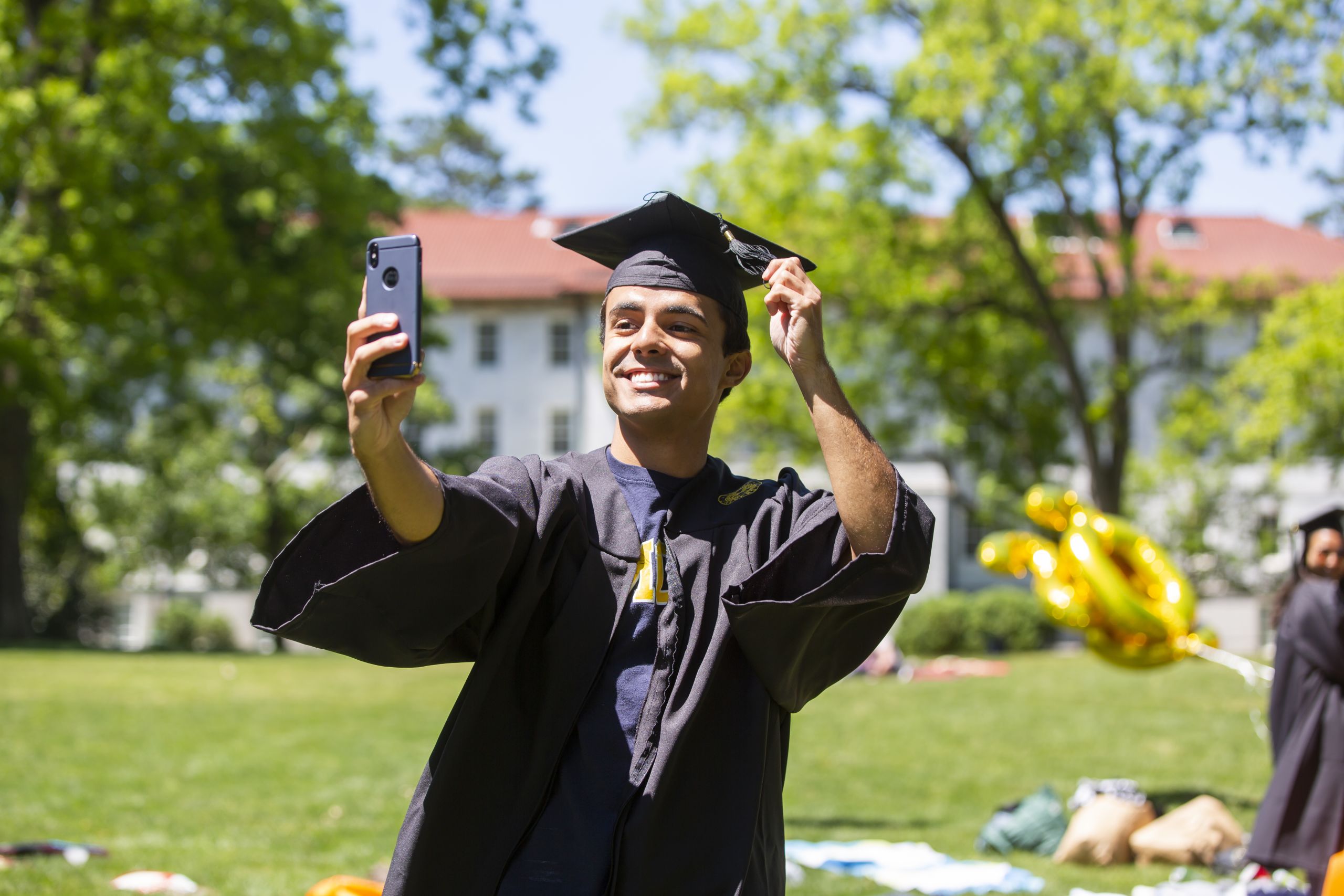 A student watches Commencement on his cell phone as he moves the tassel on his cap from right to left