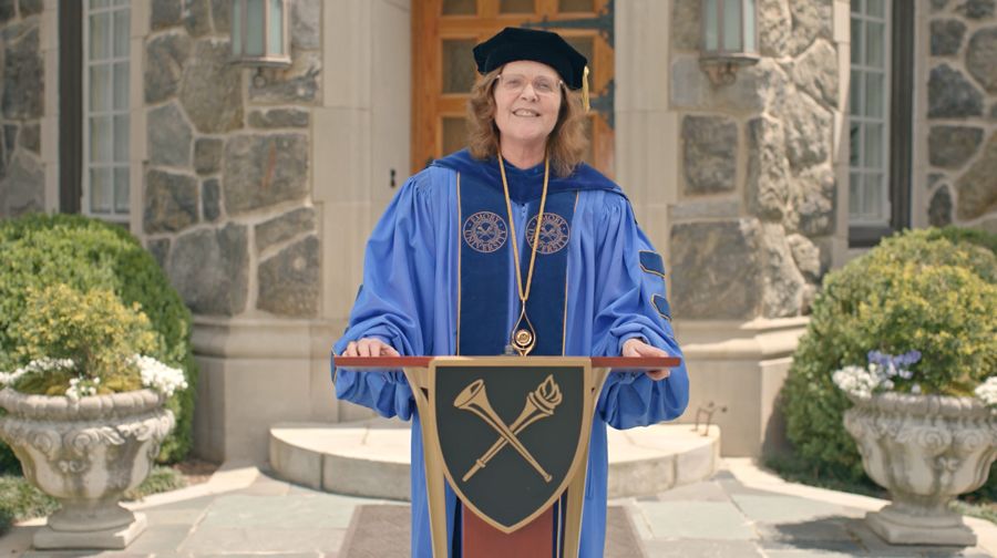 Wearing academic regalia, President Sterk stands in front of a podium.