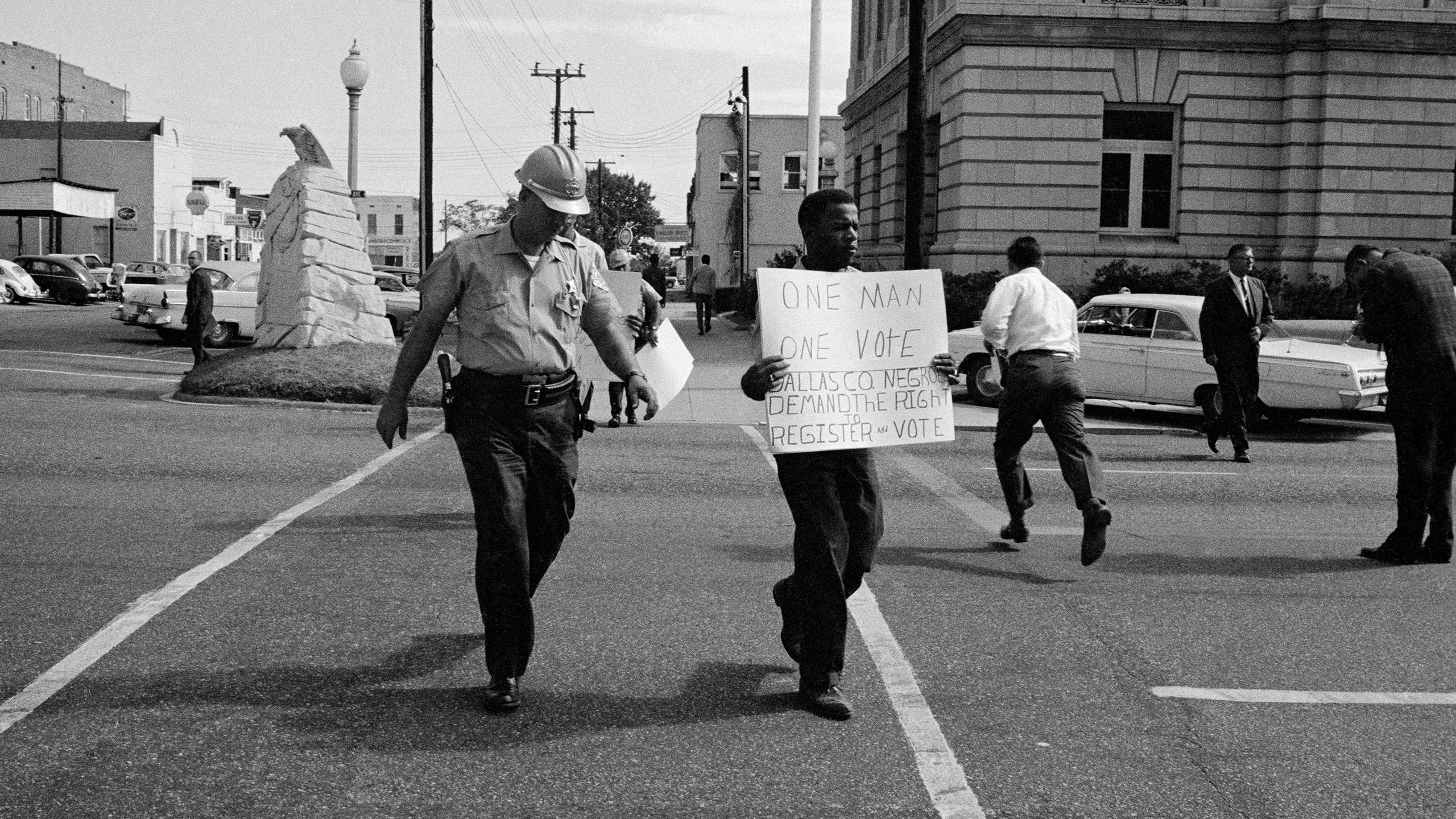 A man holds up a protest sign while a police officer walks next to him