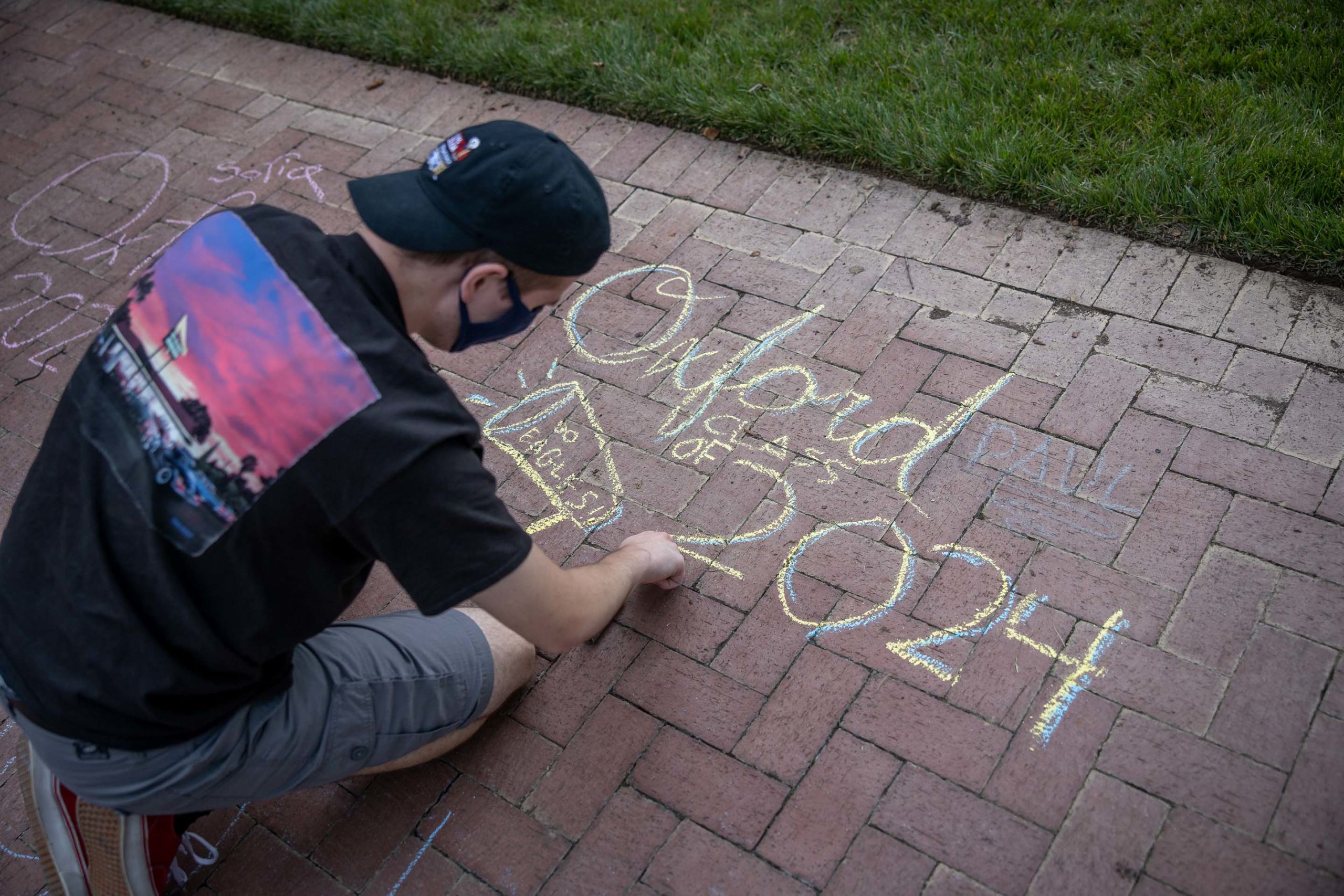 A student wearing a face covering chalks Oxford Class of 2024 on the sidewalk