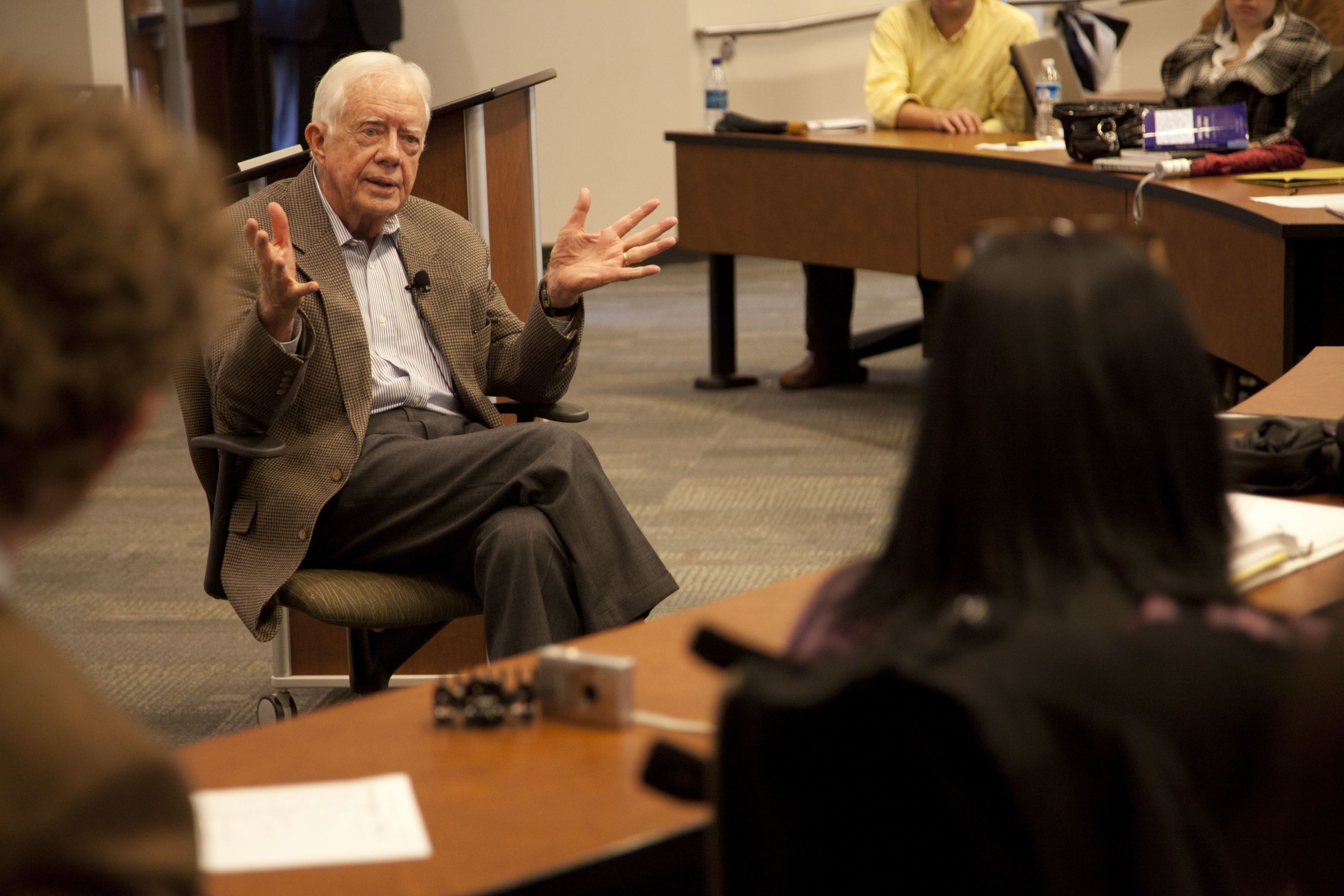 President Carter sits in a chair speaking with students in a classroom.