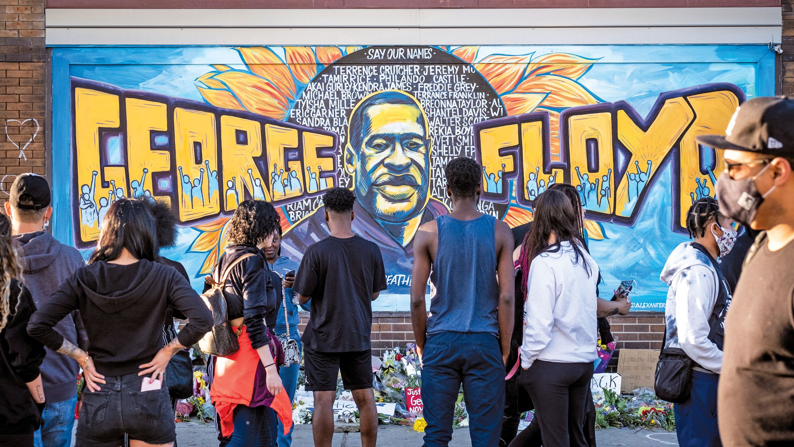 A mural of George Floyd's name and likeness with people standing in front of it. 