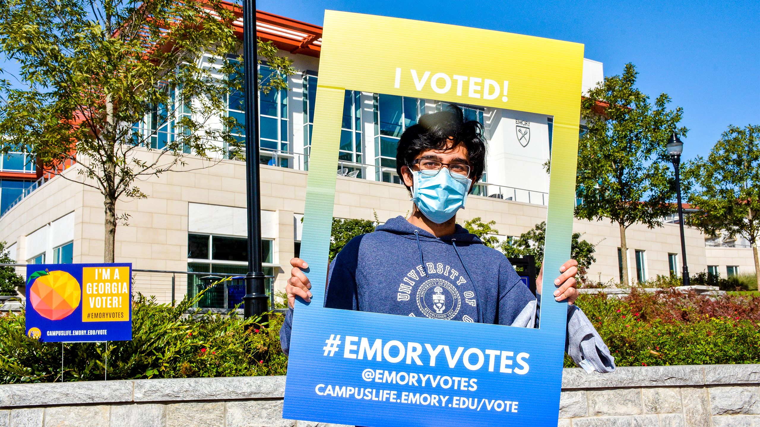 A student wearing a face covering holds a frame that says "I voted"