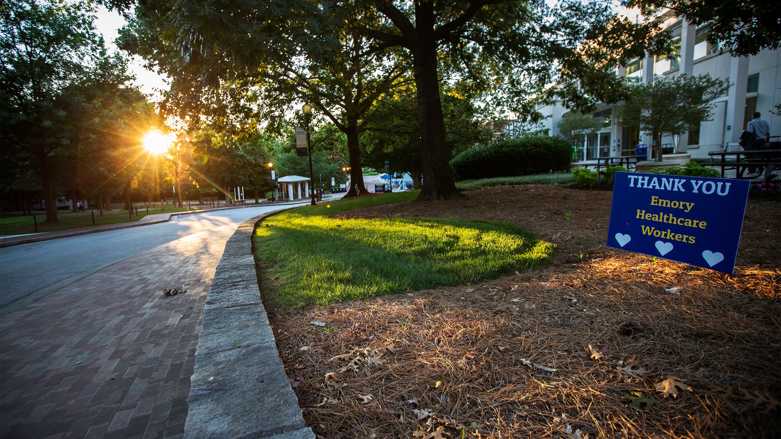 The sun sets on the Emory campus. A sign is visible reading "Thank You Emory Healthcare Workers"