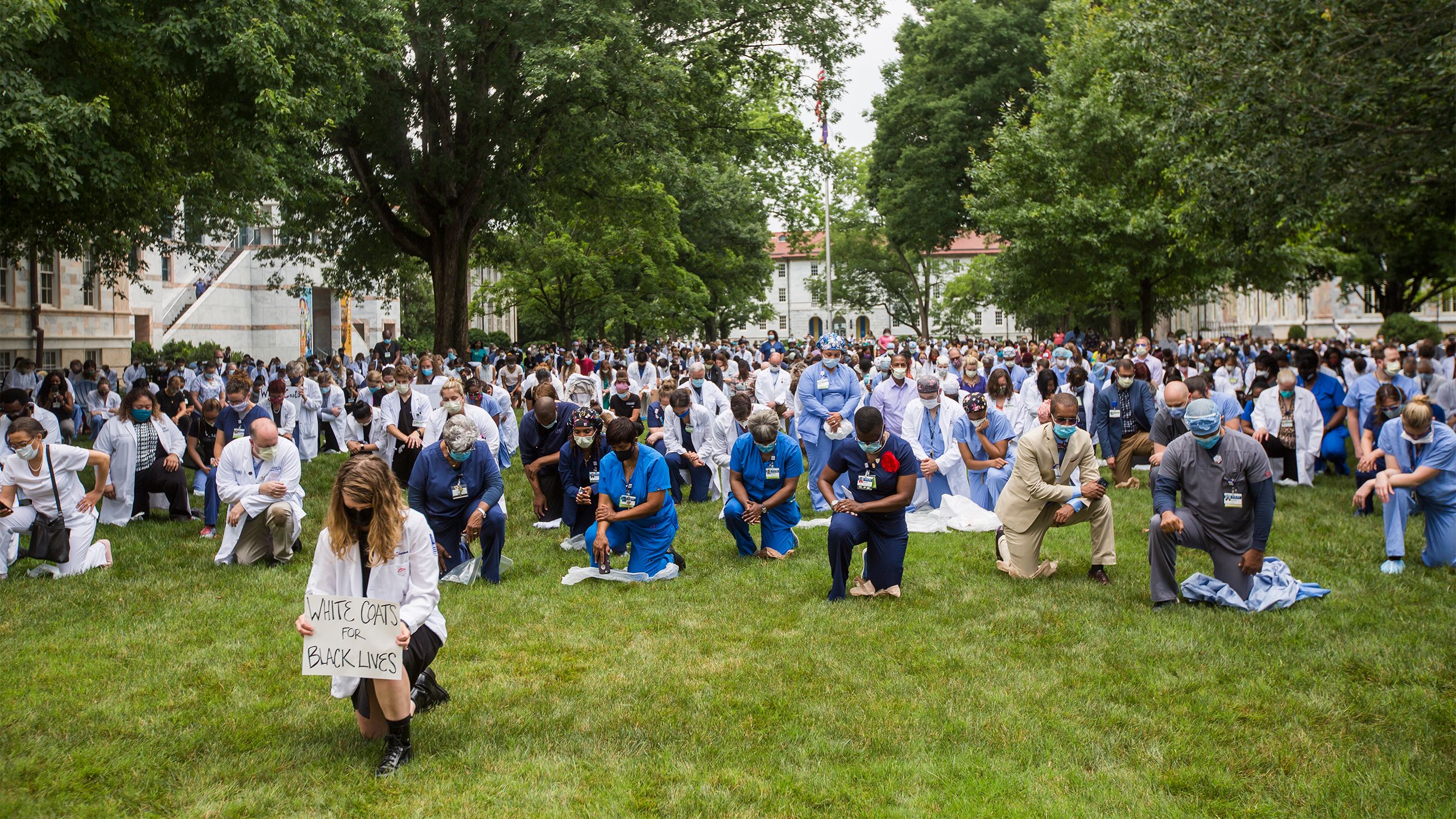 Hundreds of health care workers in white coats or scrubs kneel on the Emory Quadrangle
