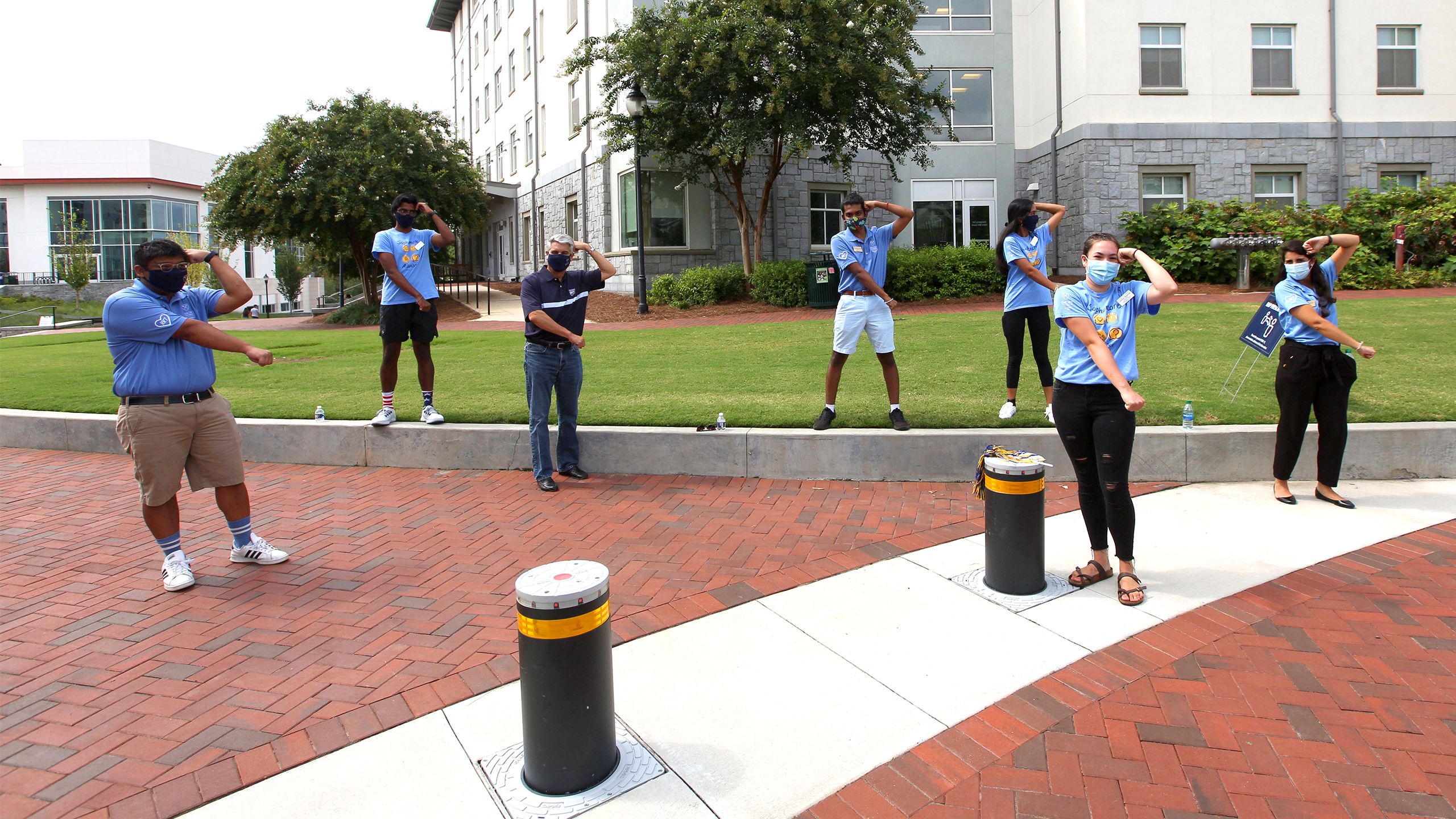 Emory President Fenves and students pose wearing masks with their arms forming the letter "R" for Emory's Raoul Hall