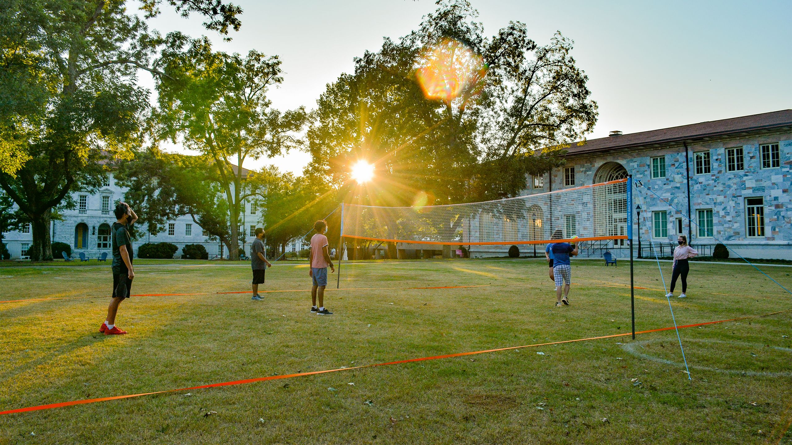 Students wearing face coverings play volleyball on the Emory quad as the sun sets
