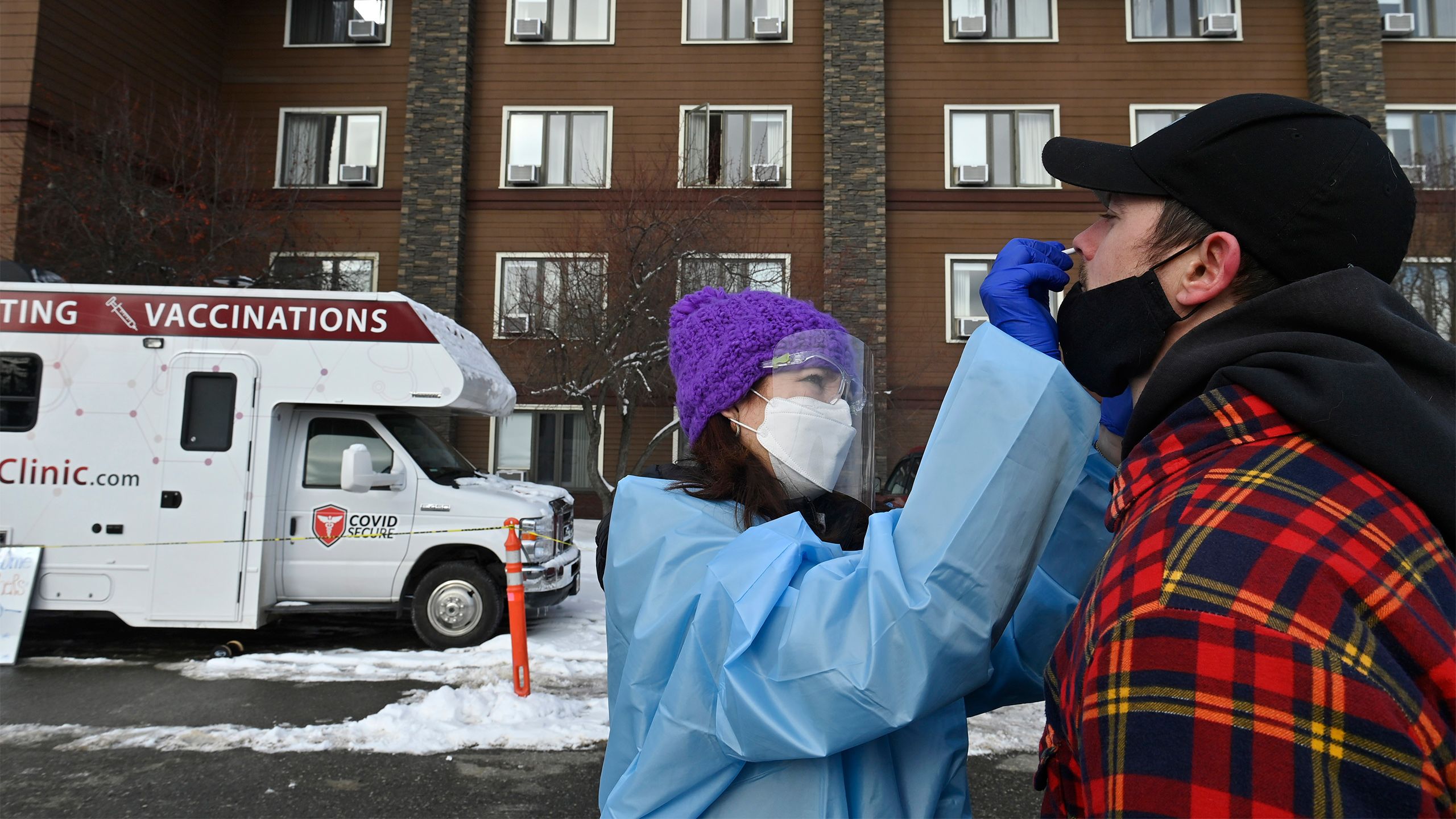 Wearing a face mask, face shield and protective gown, along with a warm winter had, Jodie Guest swabs the nose of a man preparing to compete in the Iditarod