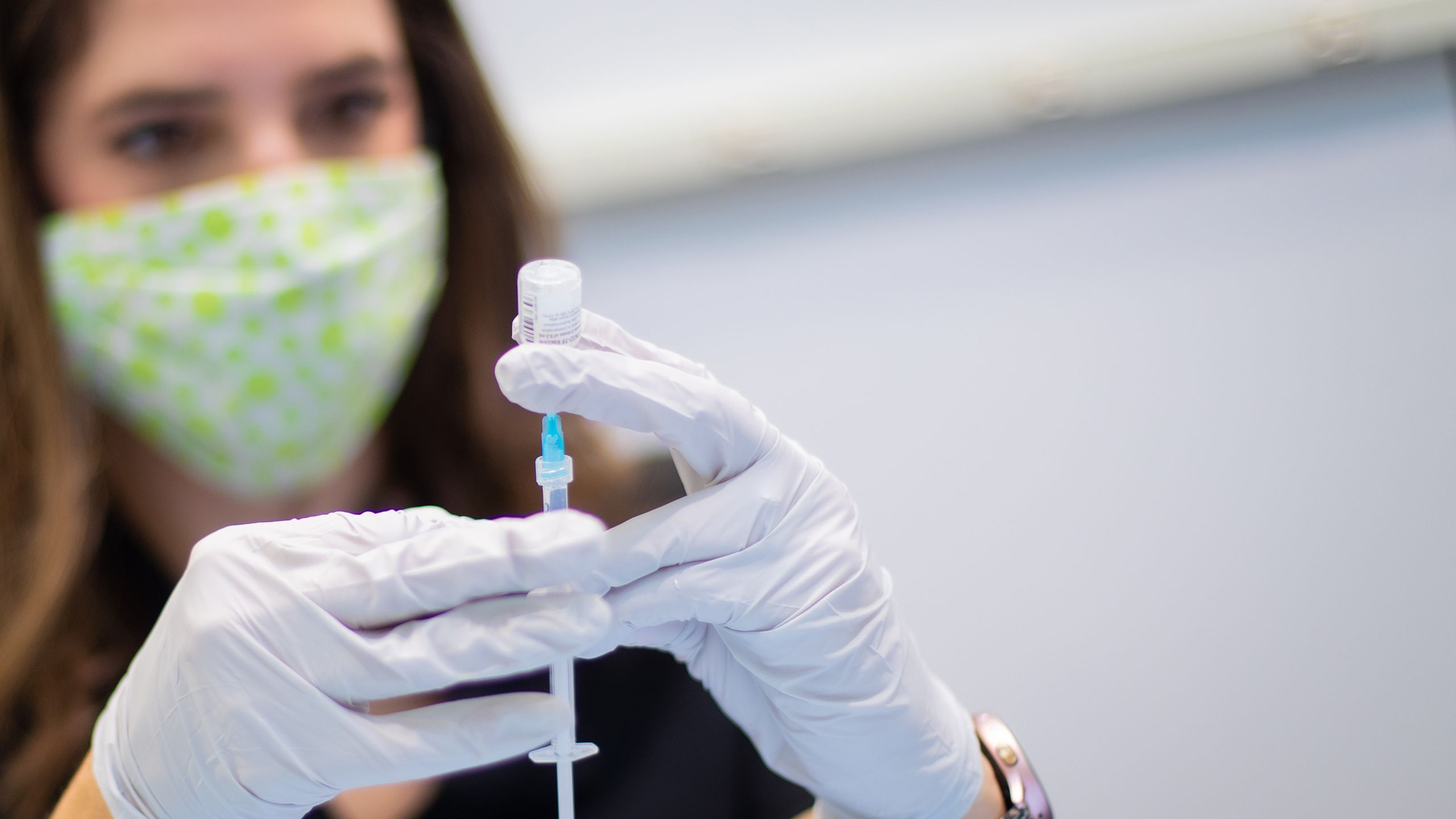 A woman in a mask and gloves draws a vaccine does into a syringe from a vial