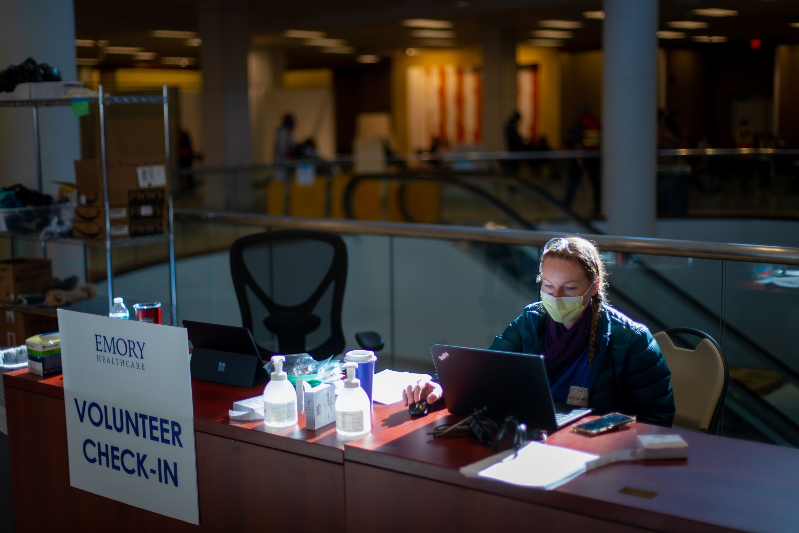 a woman in a mask works at a desk with a laptop to check in volunteers