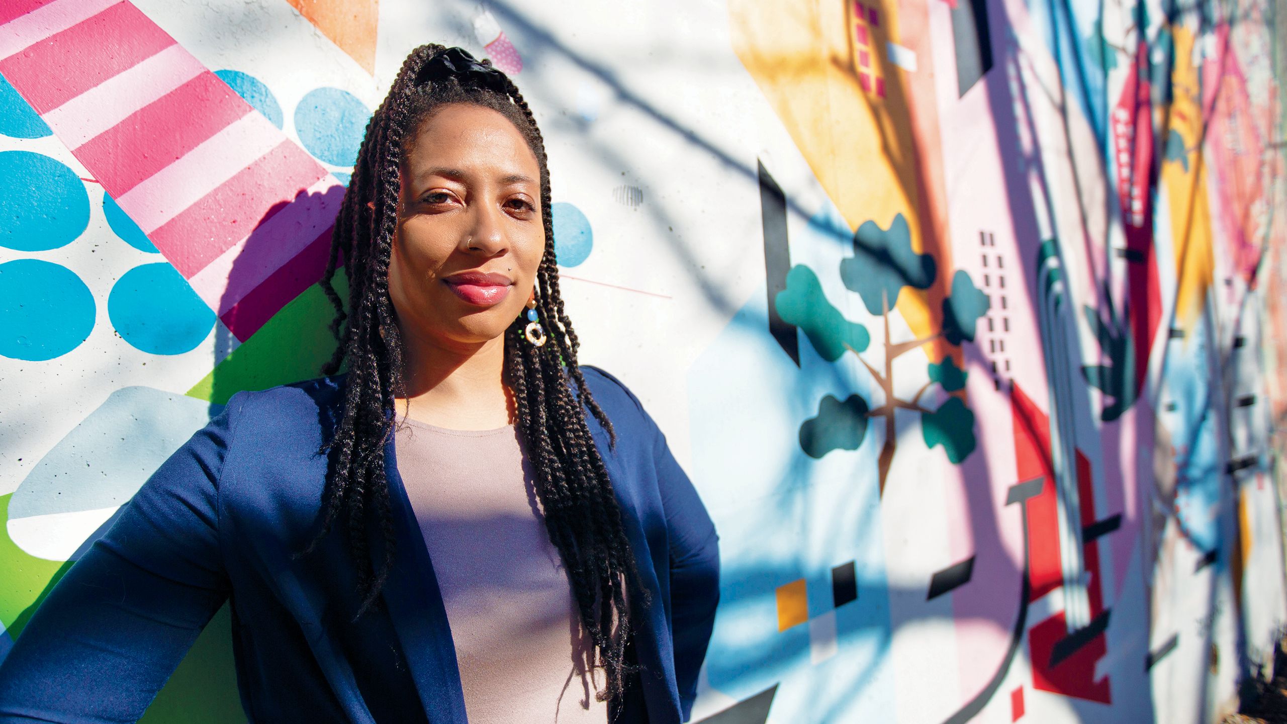a photo of izarelle mckinnon standing in front of a colorful abstract mural by Joe Camoosa.