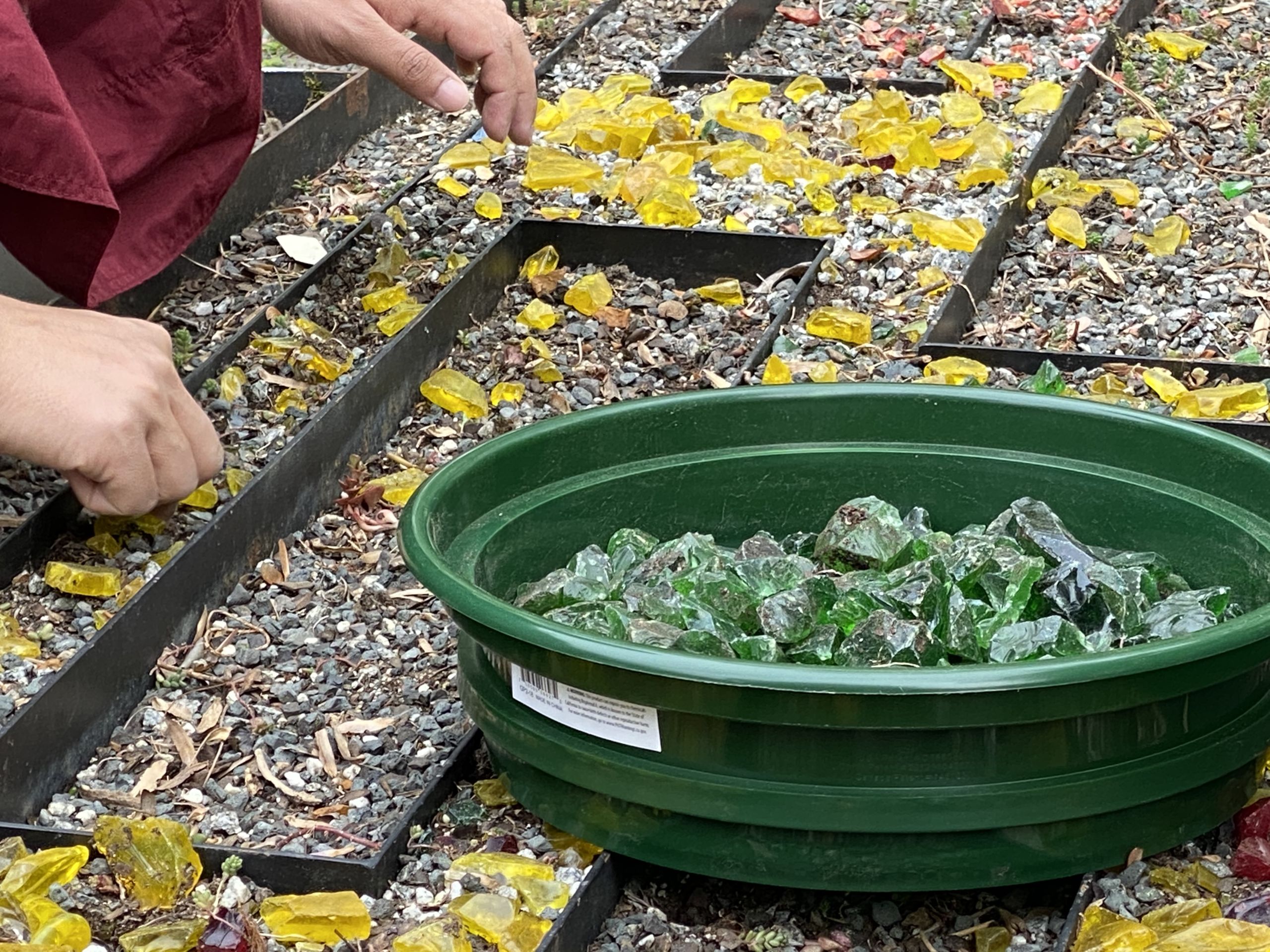 A close up of a bucket of colored glass being removed from the living mandala