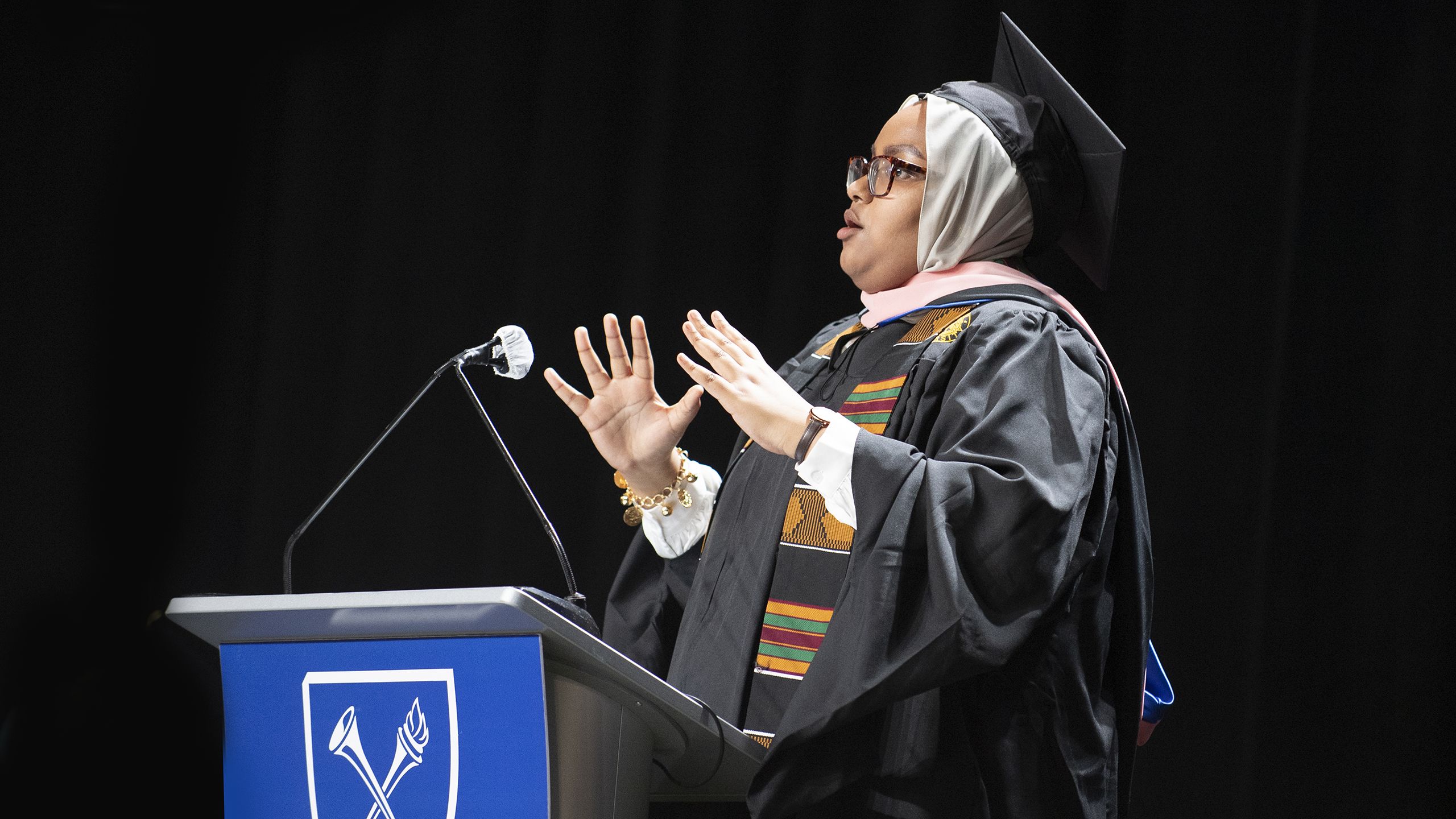 A graduate in cap and gown speaks at a podium