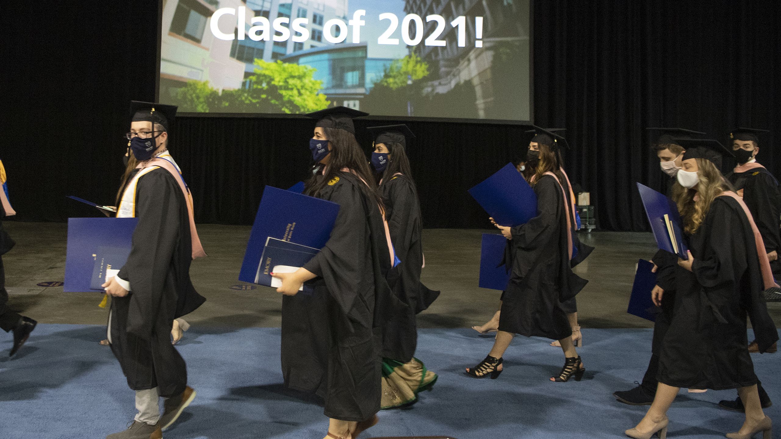 graduates in caps and gowns carry their diploma folders