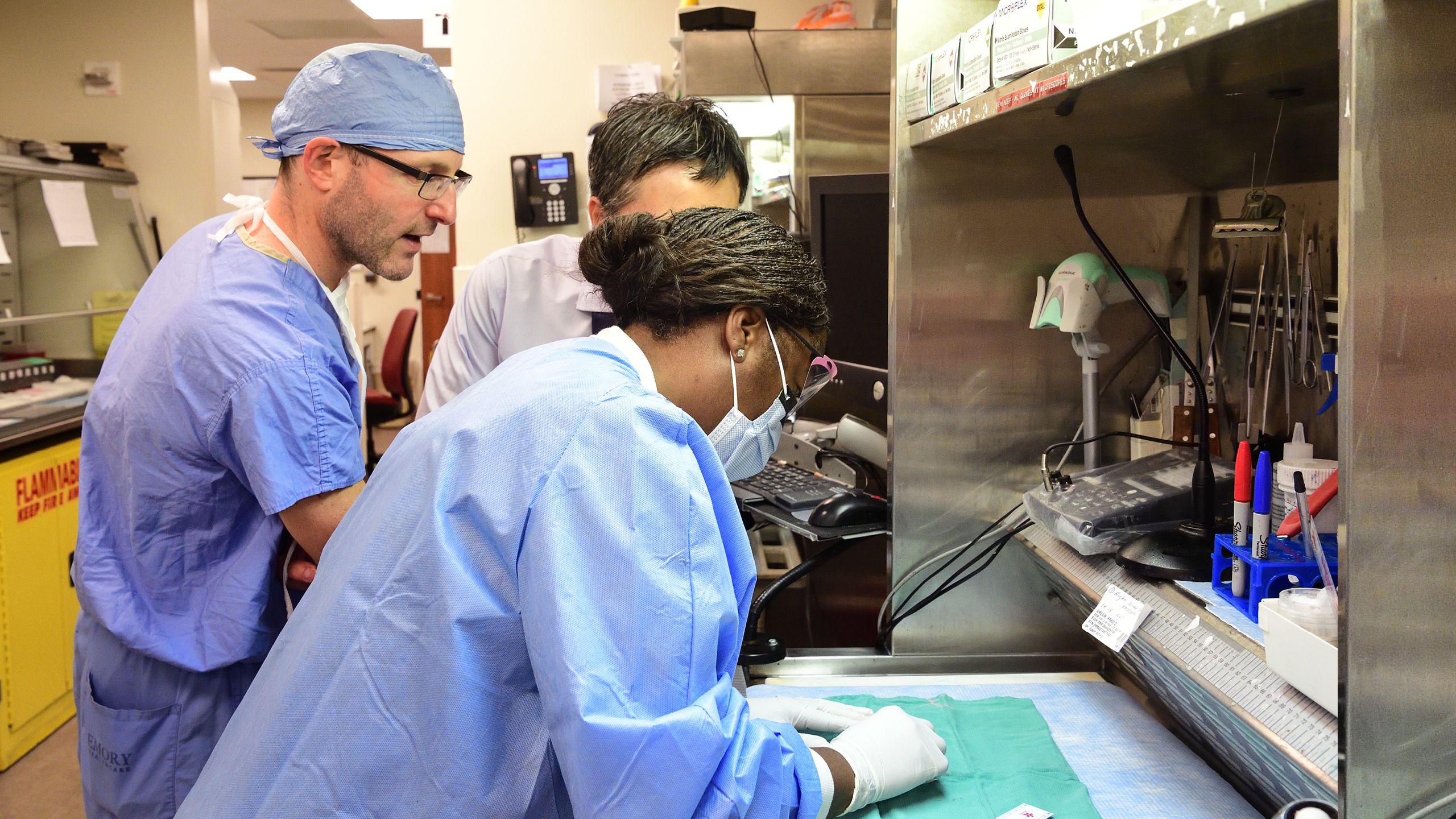 Three medical team members reviewing information in a huddle. The doctor has on blue scrubs.