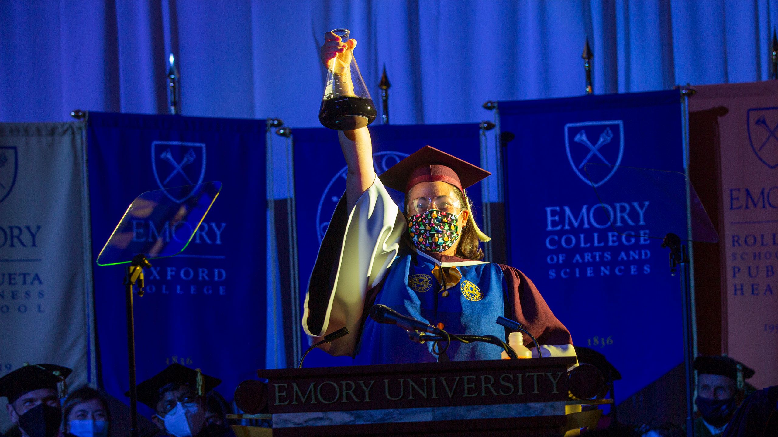 Emory faculty member Tracey McGill holds up a beaker with a liquid that changes from gold to blue
