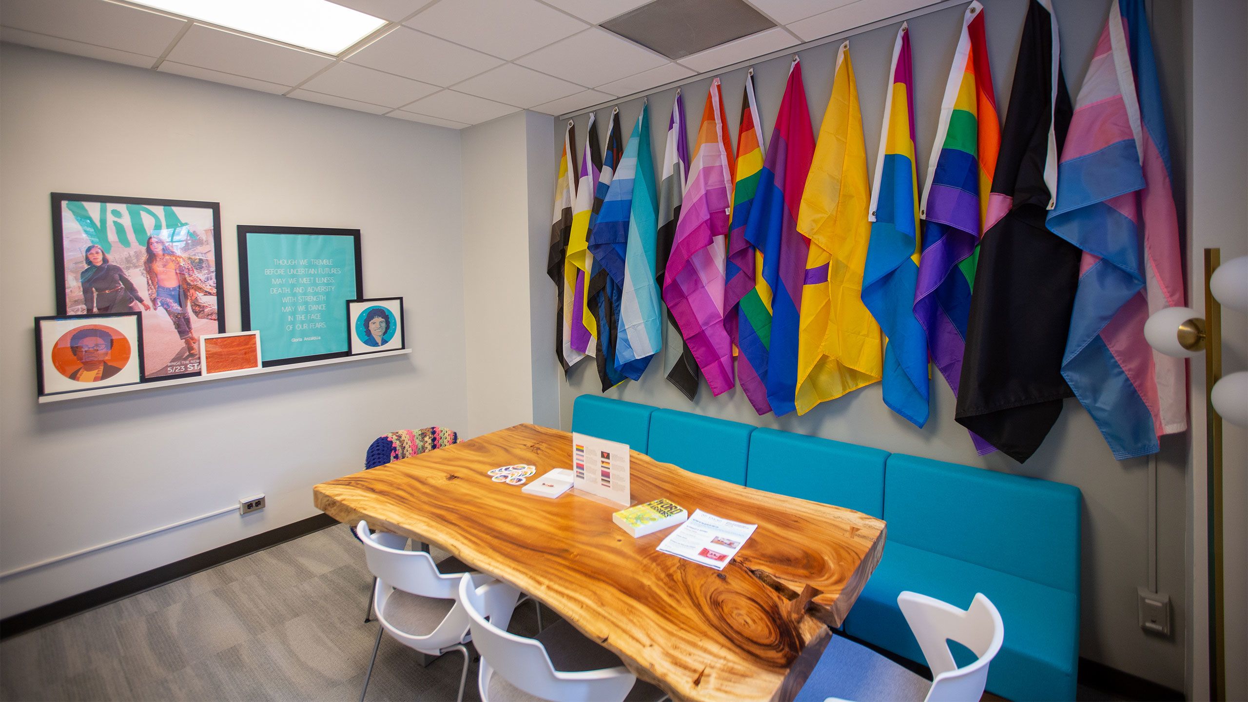 Flags hang on a wall behind a couch and wood table in the Office of LGBT Life