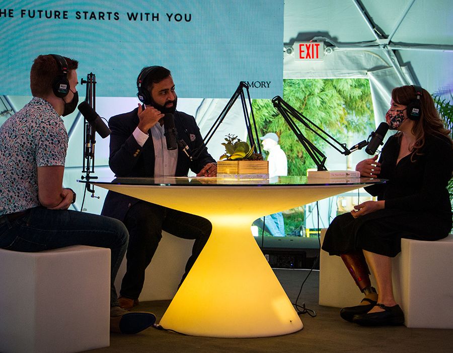 Professor Cassandra Quave records a podcast with student Cutler Cannon, hosted by Munir Meghjani (center), president of the Emory Alumni Board, sitting around a lighted table with microphones and headphones.