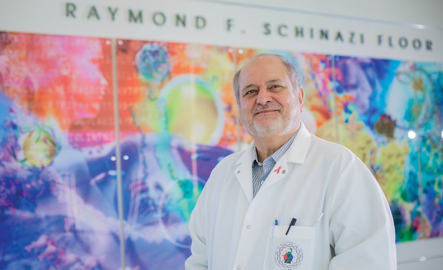 a portrait of raymond schinazi standing in front of a colorful health science mural.