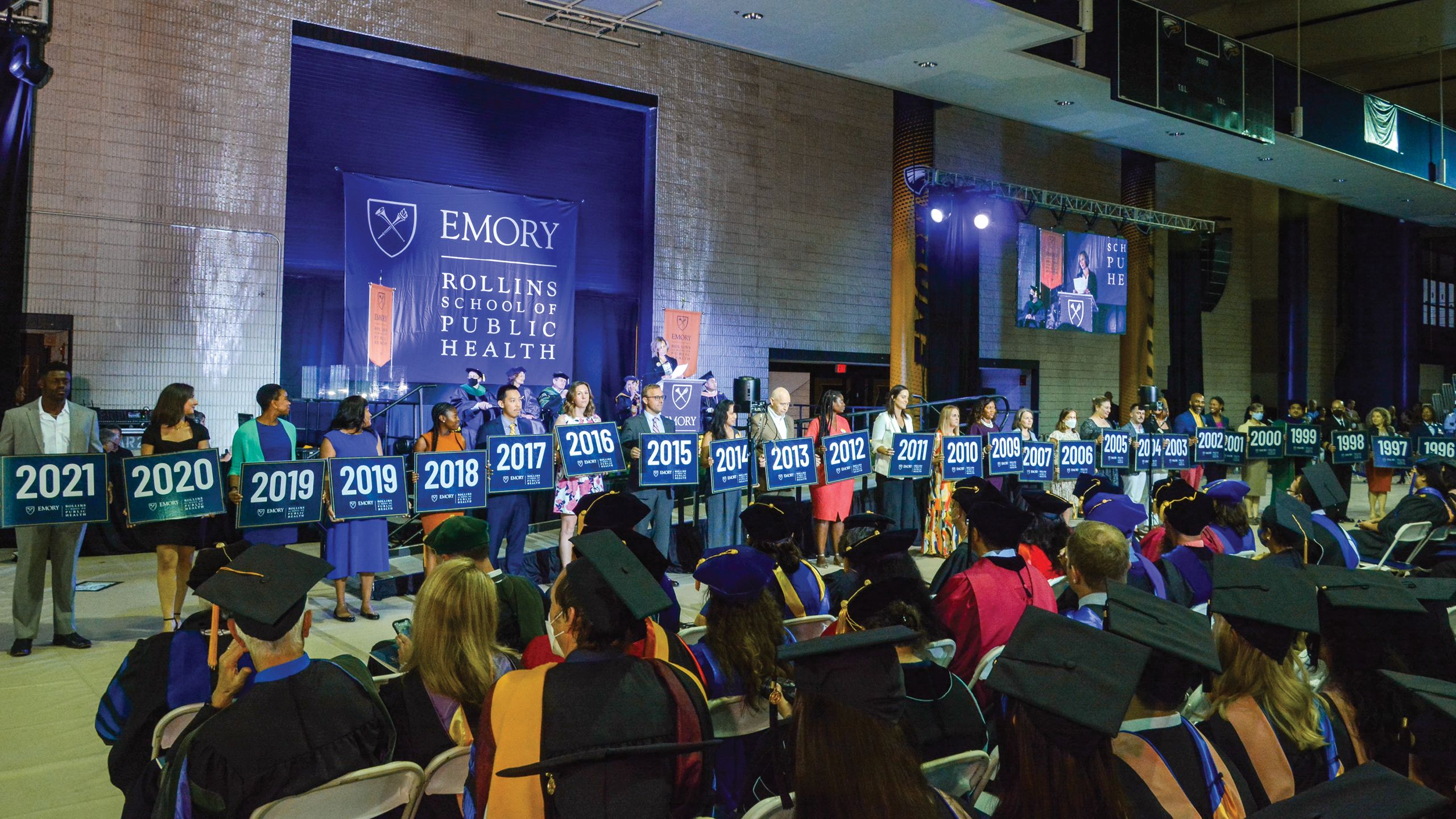 A line of people, each holding a large blue card with a white year printed on it, starting at 2021 and going downward, like the stage at the Rollins commencement ceremony.