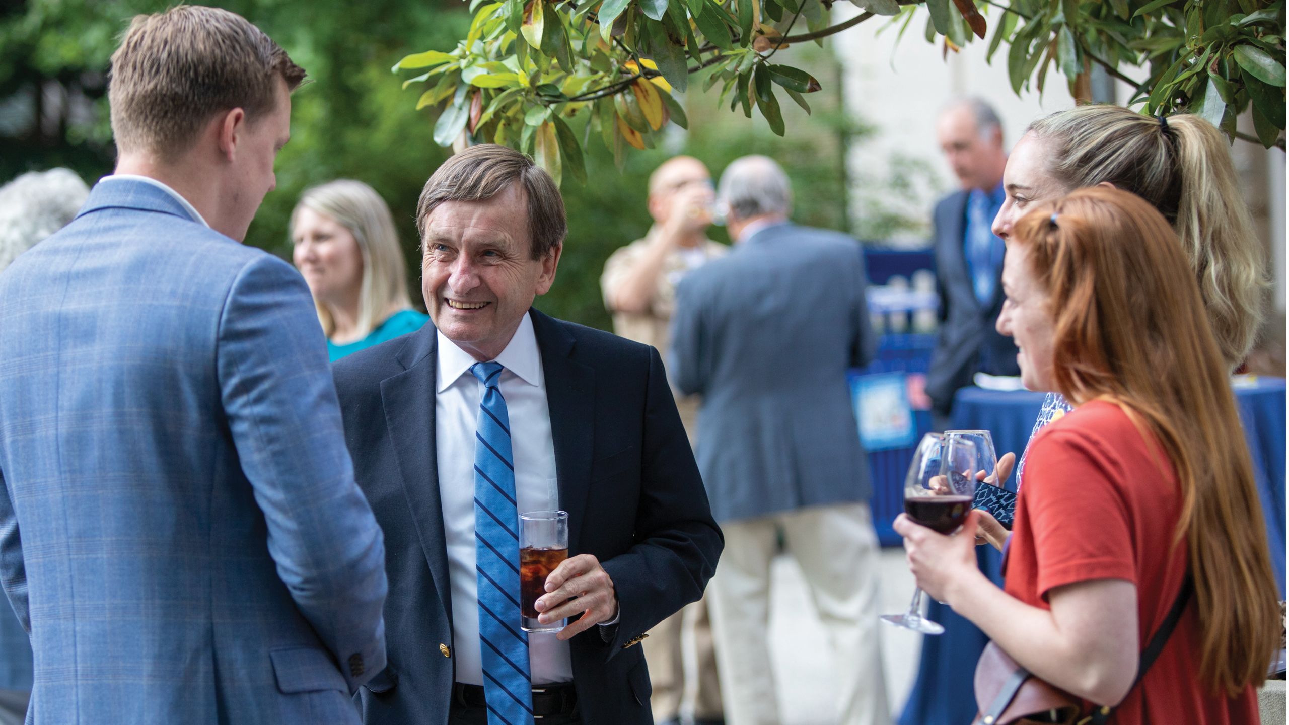 A man in a coat and tie talks to other people