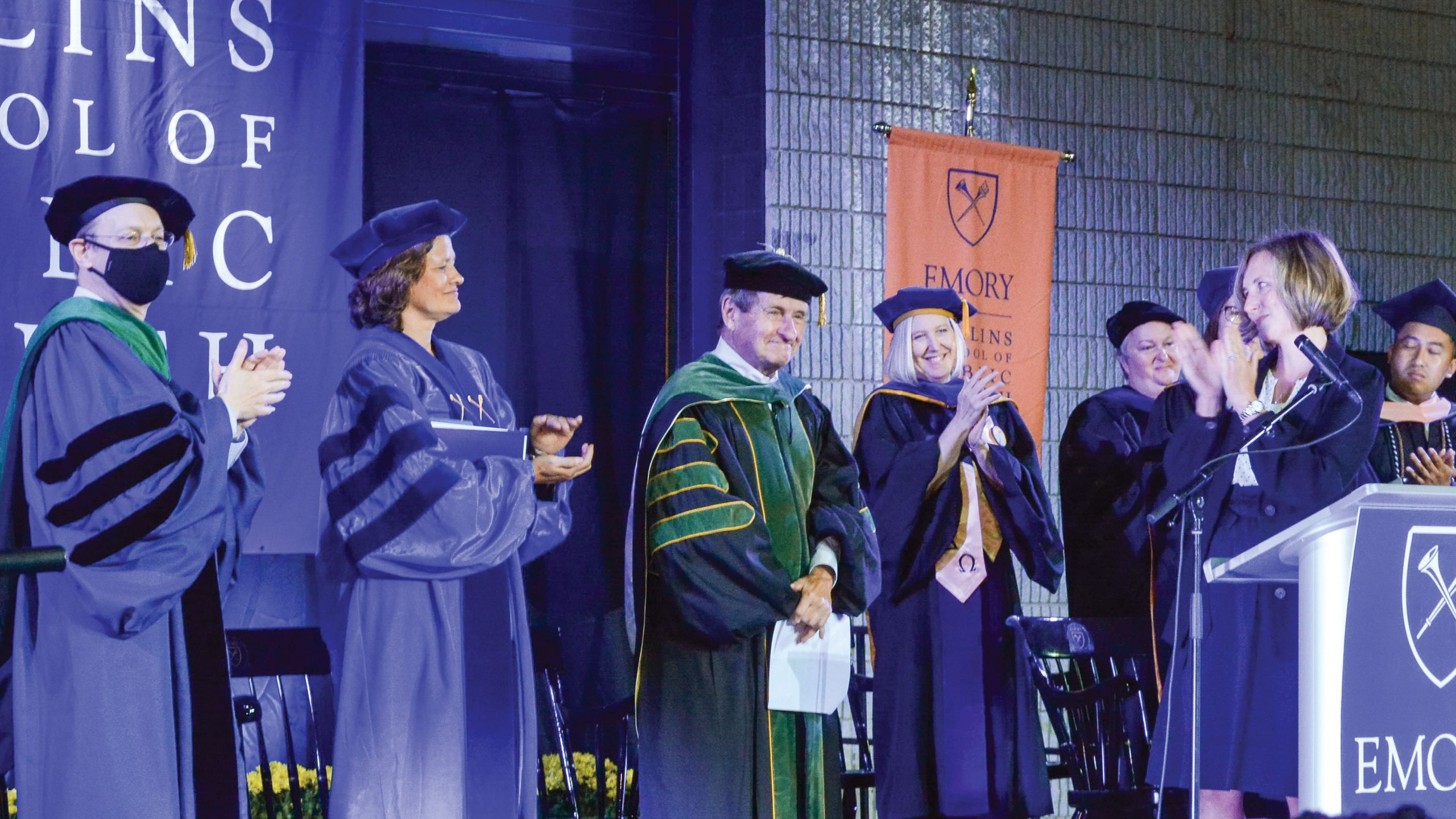 People in commencement regalia applaud a man, also in commencement regalia.