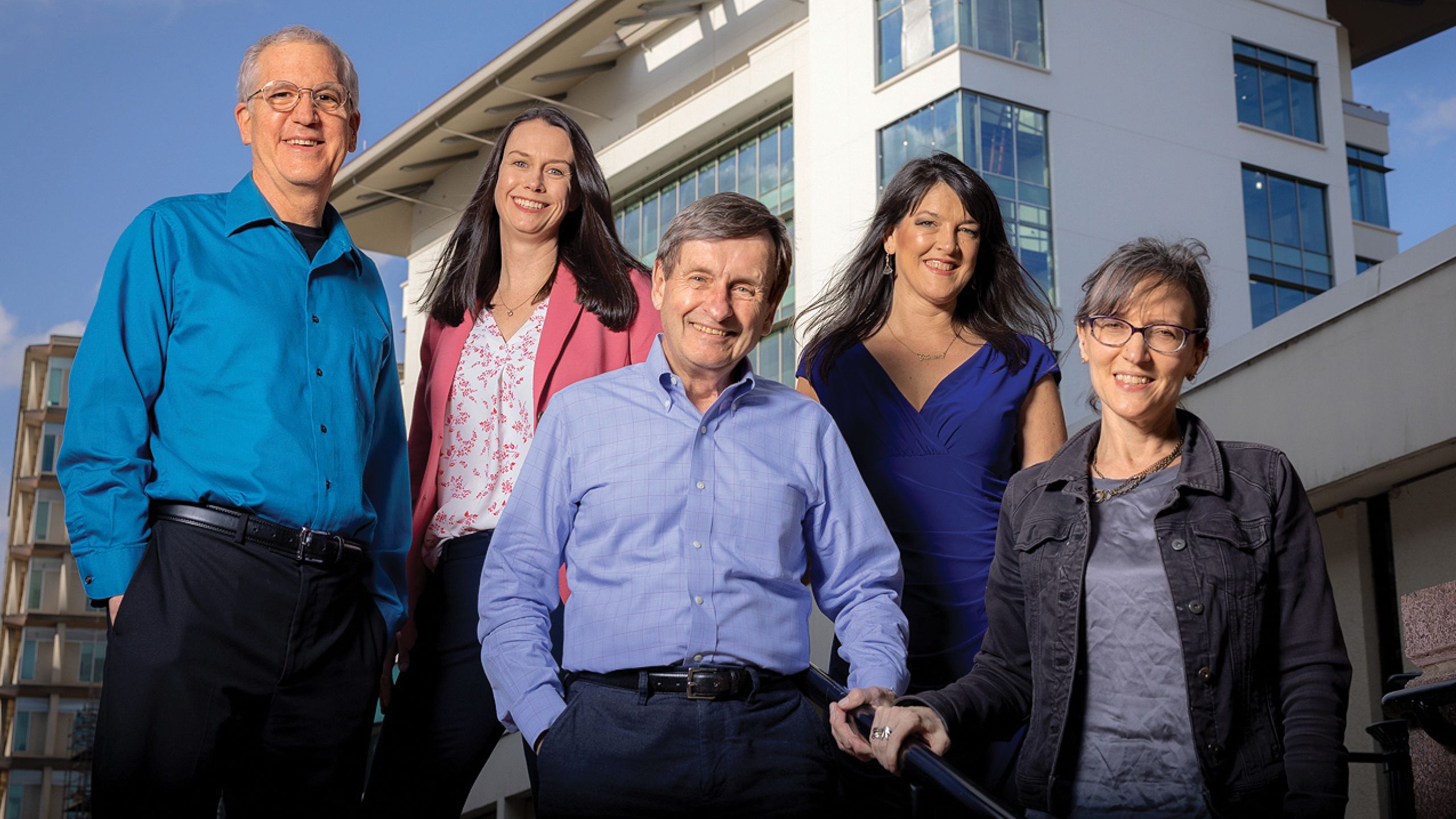 A GROUP OF 5 PEOPLE STANDING IN FRONT OF THE CAMERA SMILING.