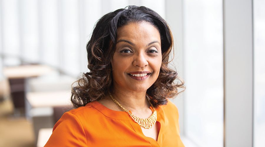 A head shot of a woman in an orange blouse and gold necklace.