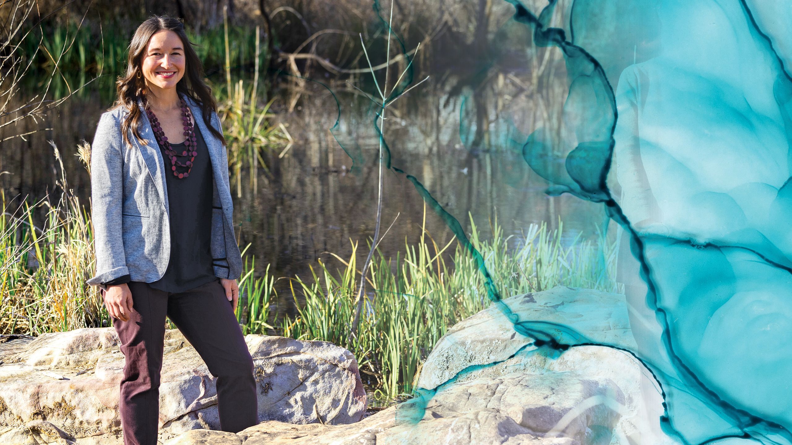 A photo of a young woman standing on a rocky lake shore.