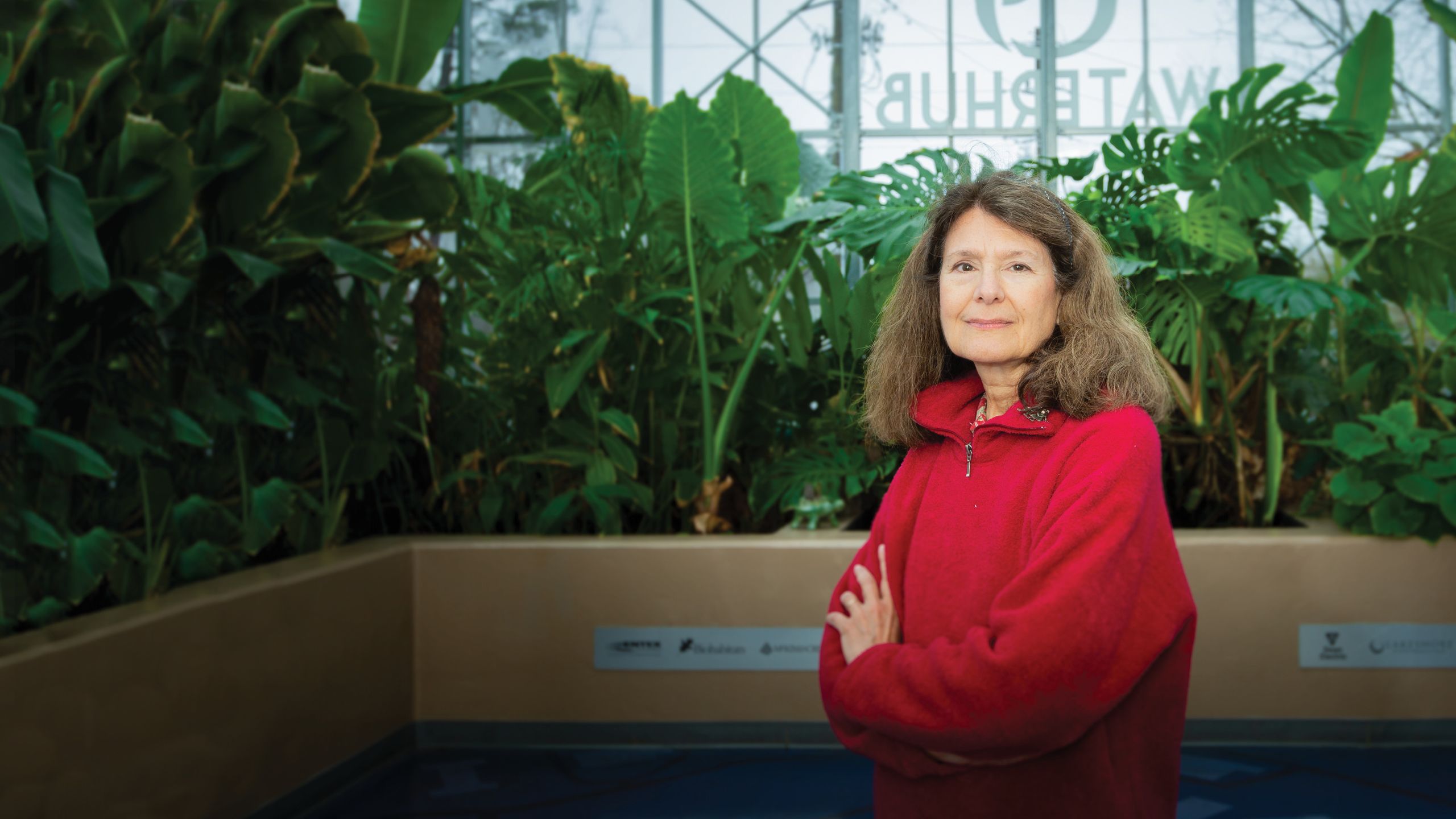 A photo of a woman standing in front of plants smiling for the camera.