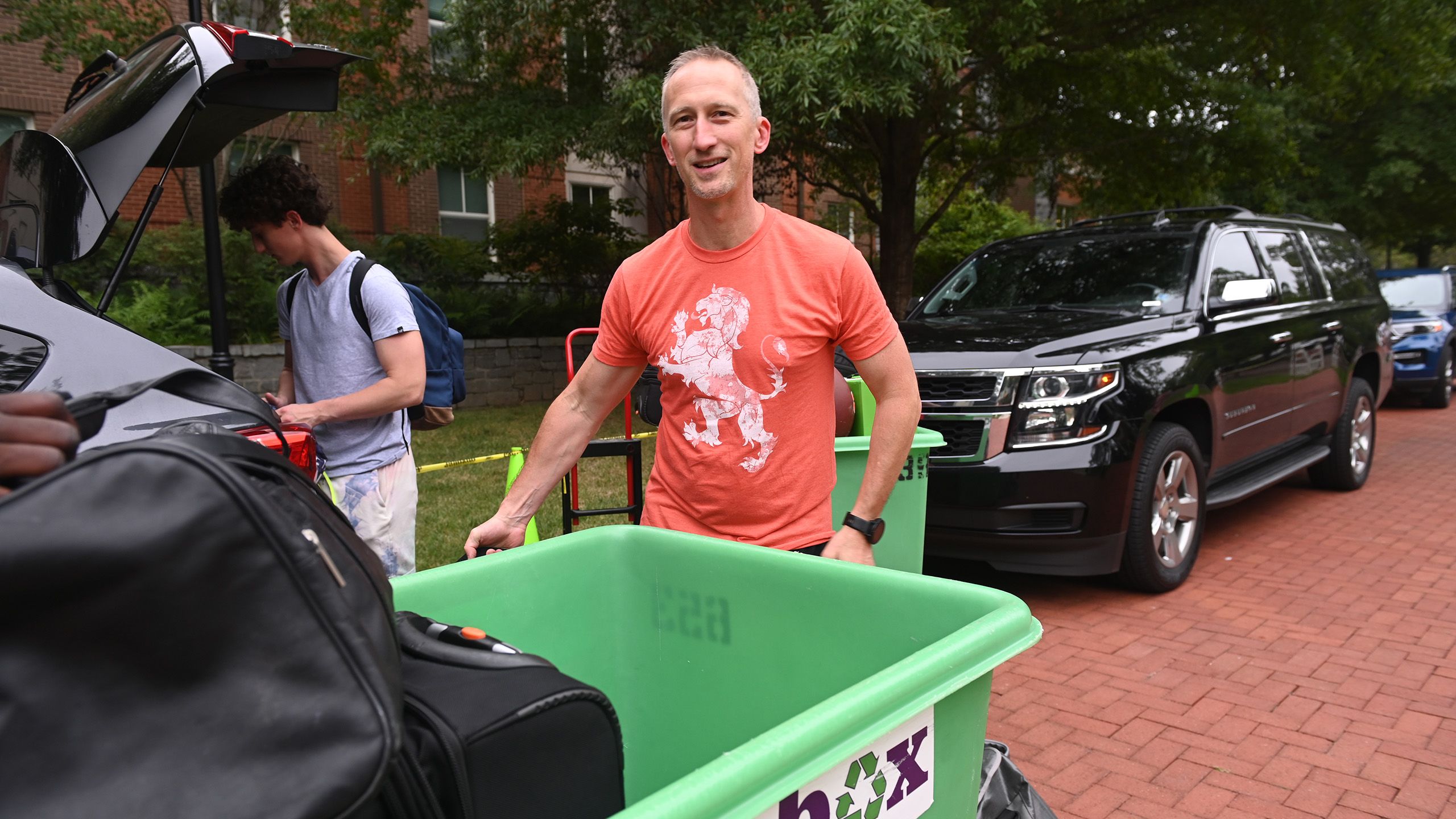 Dad helping his son unpack his luggage from the car.