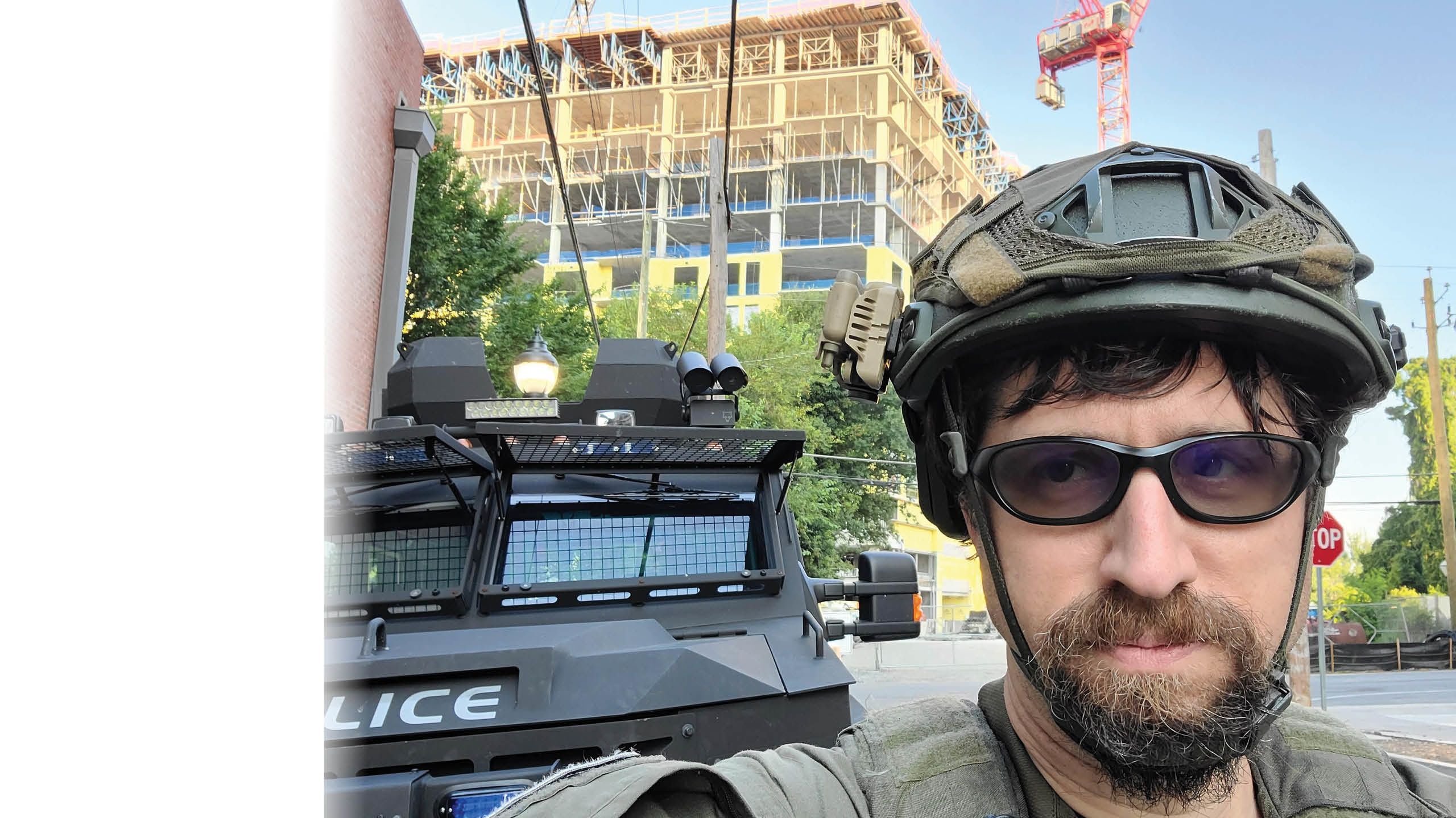 A man in a SWAT helmet standing with a city street background.