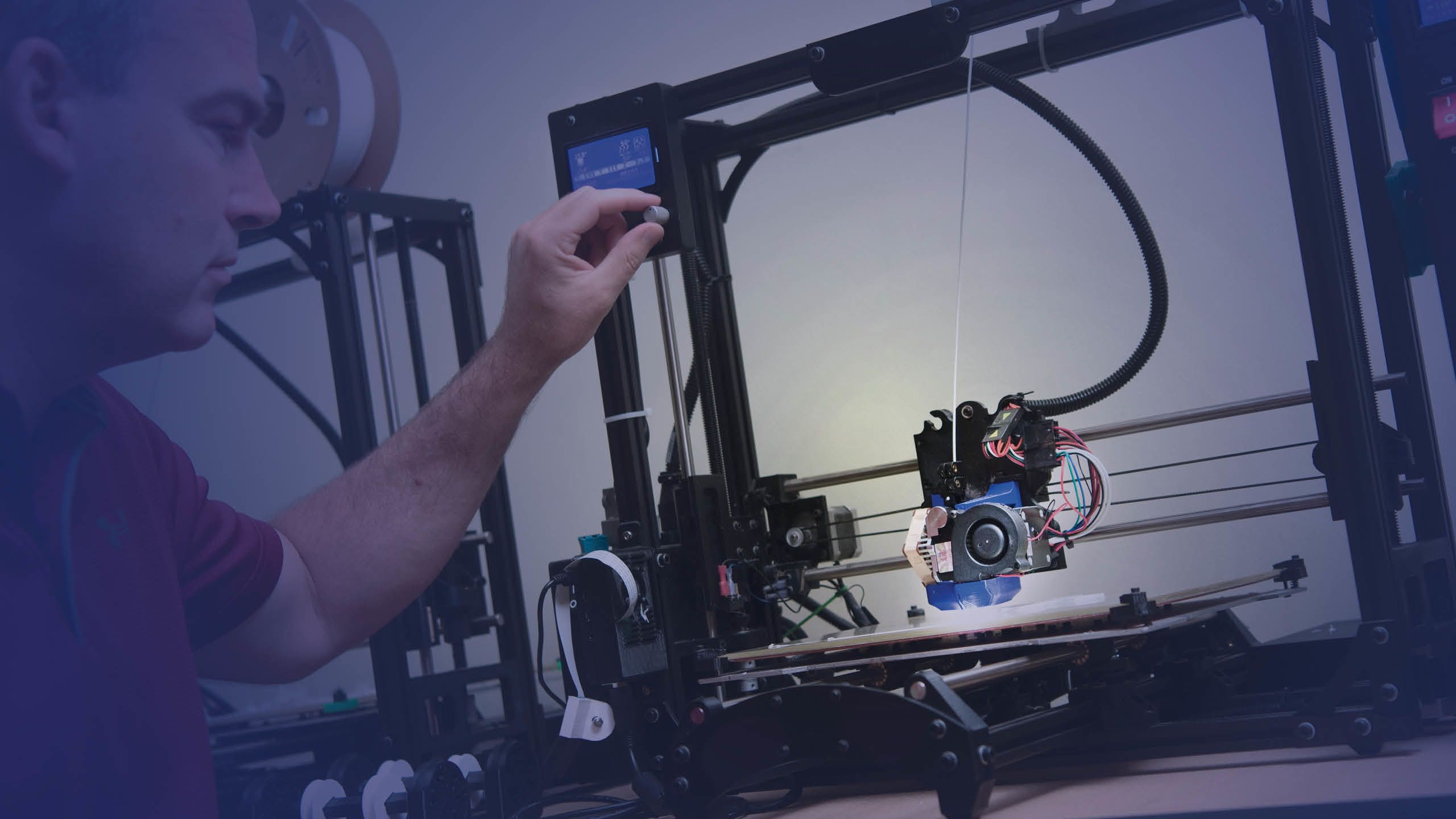 A photo of a man operating a 3-D printer.  