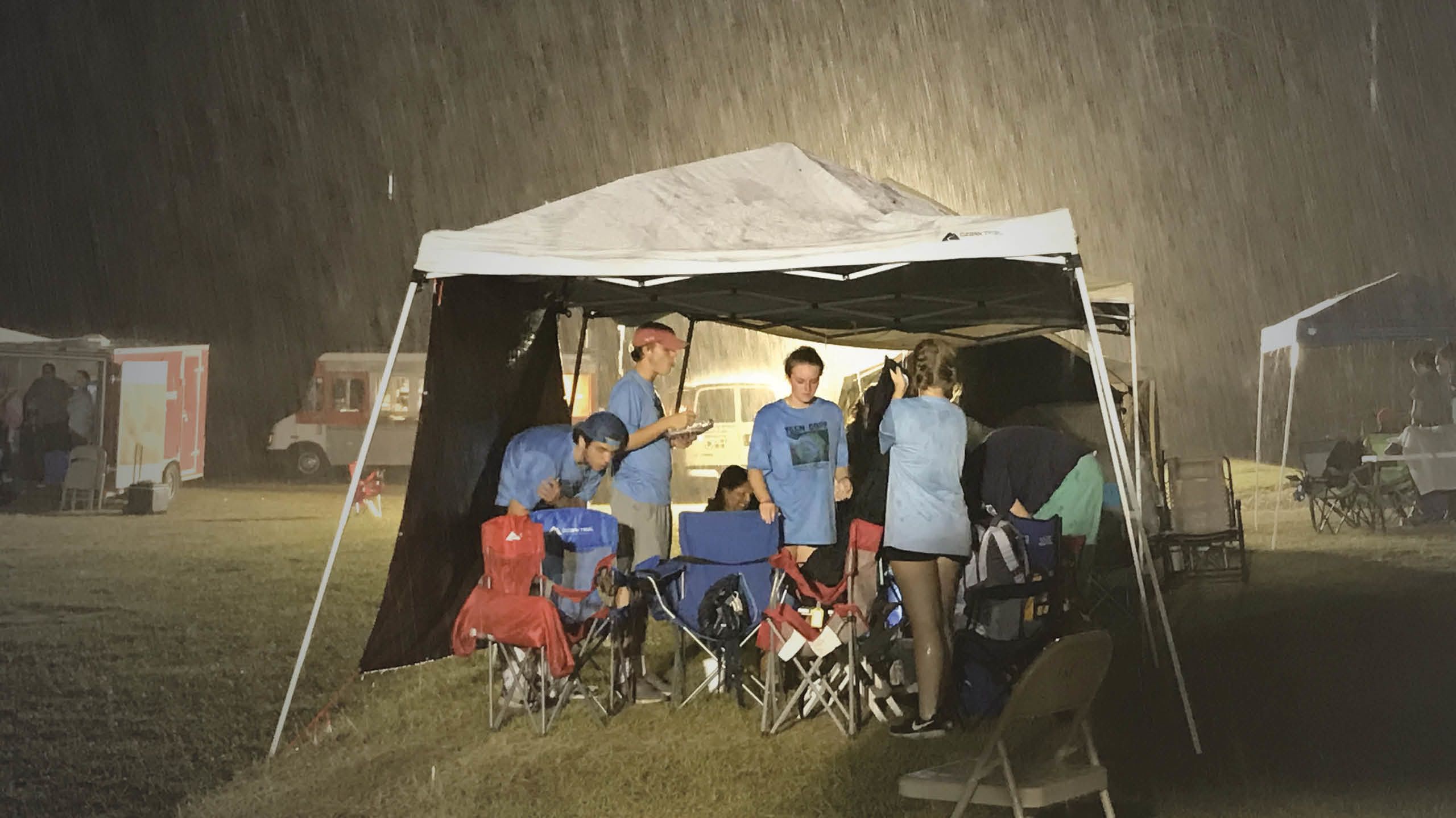 A group of physician assistant students under a tent in the rain.