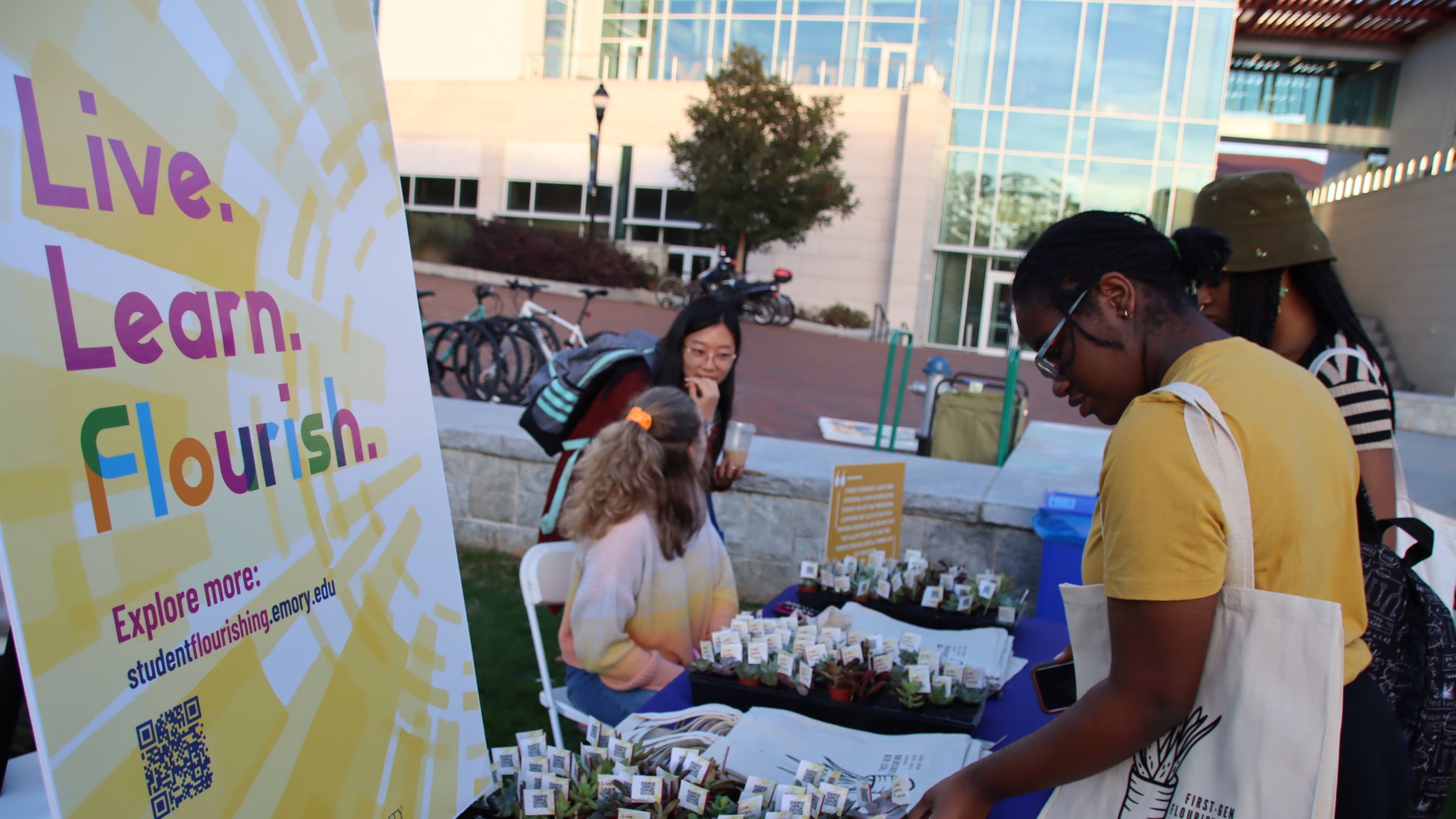 Students visit a table with a sign that says "Live, Learn, Flourish"