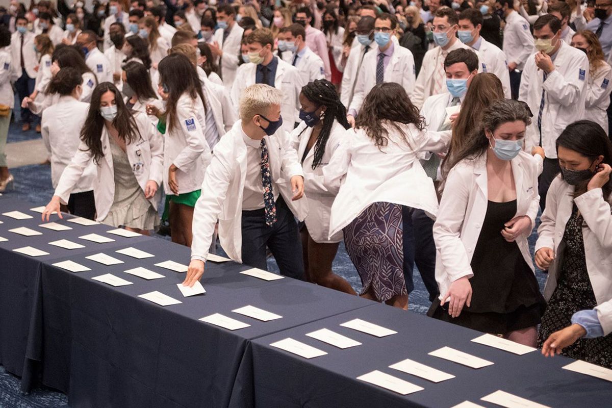 Students in white coats crowd around a table filled with envelopes