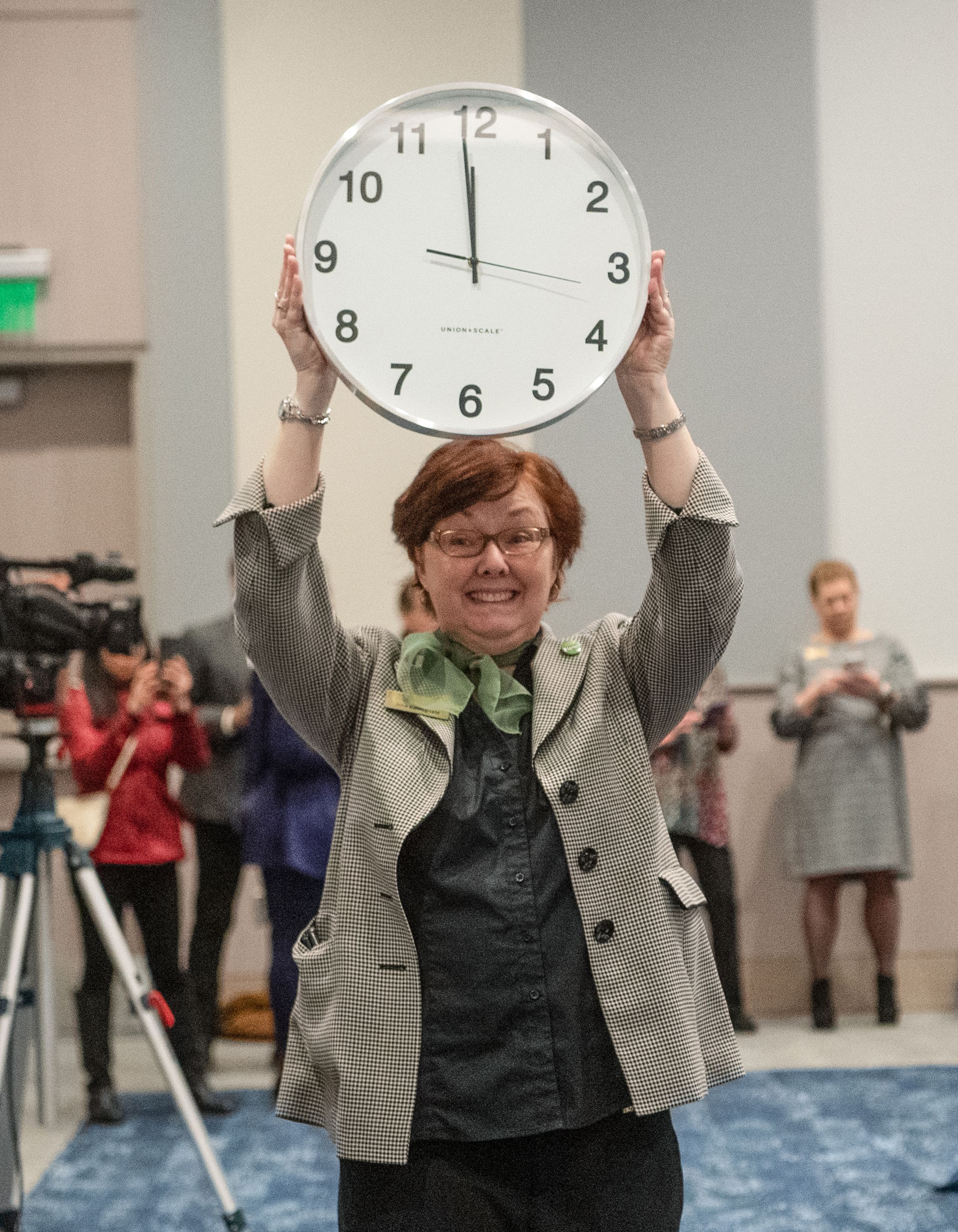 A woman holding a large clock with hands almost at noon