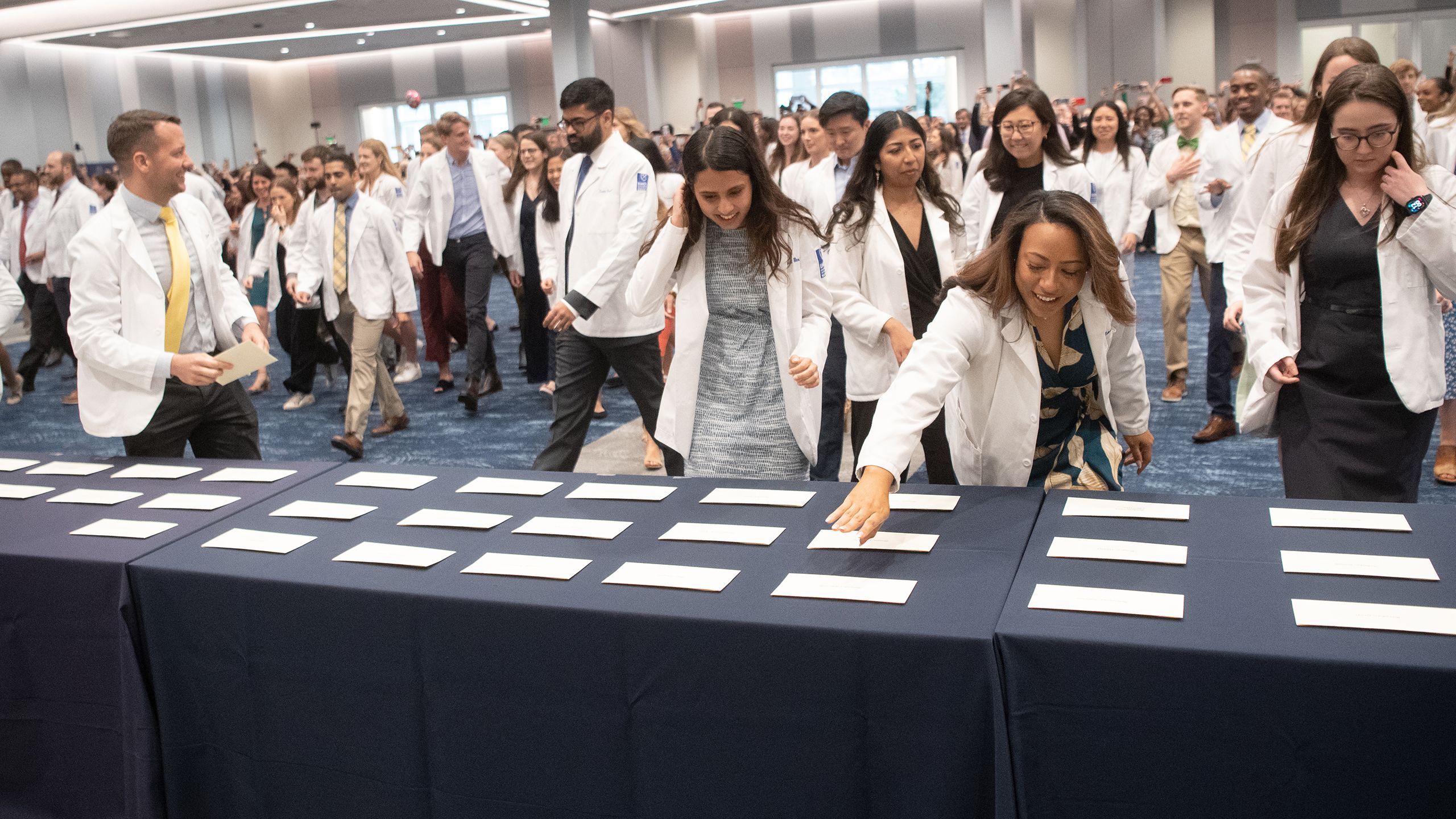 Students in white coats race forward to pick up white envelopes off a table