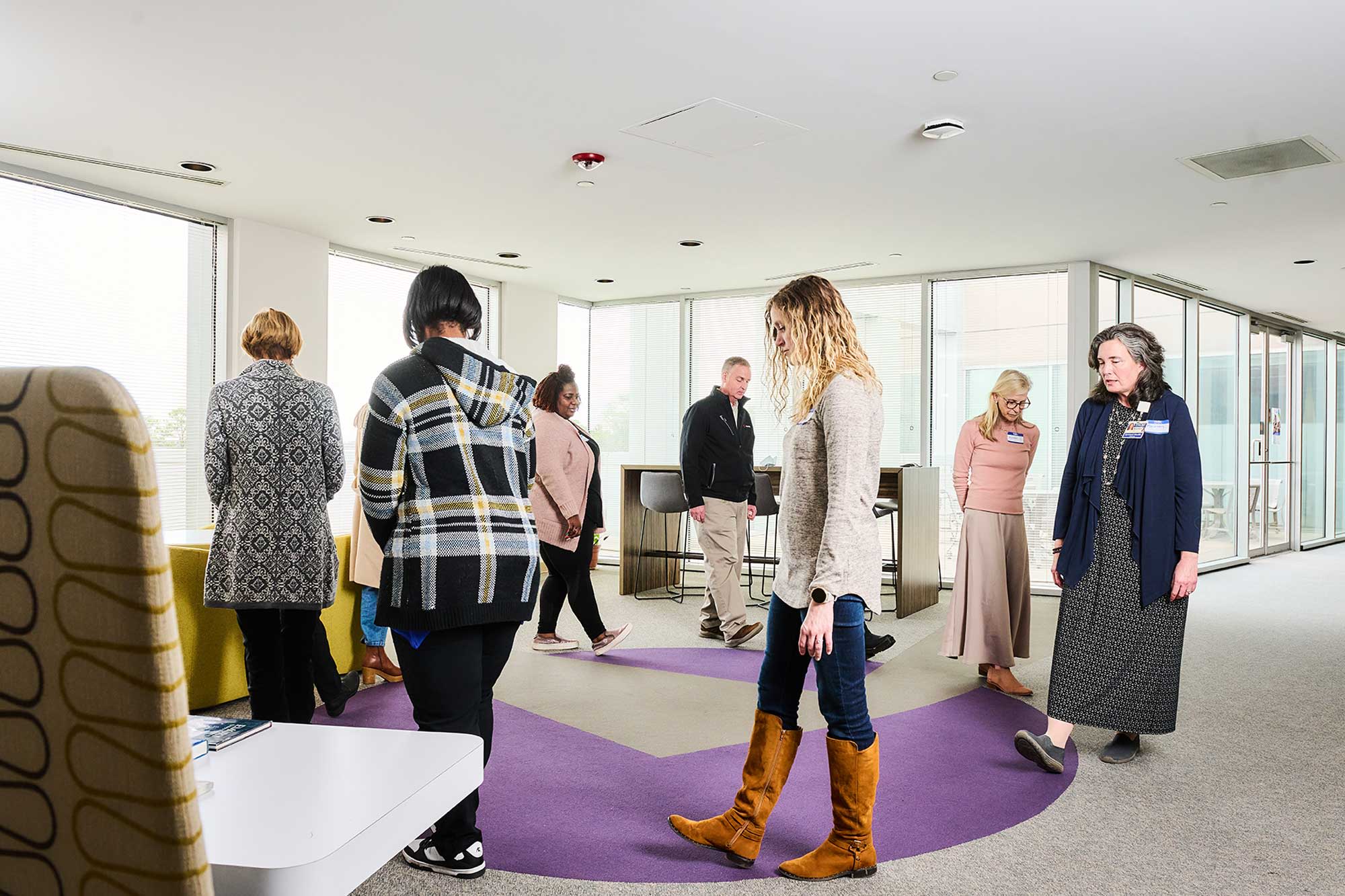 Participants walking in a circle in an open interior space with large windows and purple and gray carpeting