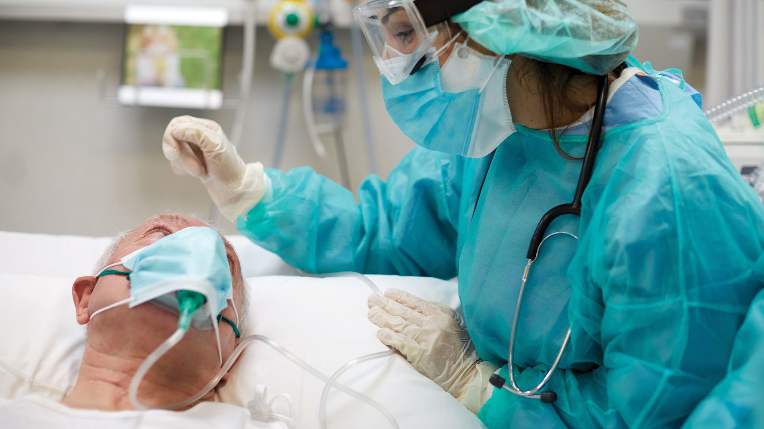 A nurse interacts with a patient in a hospital bed receiving oxygen.