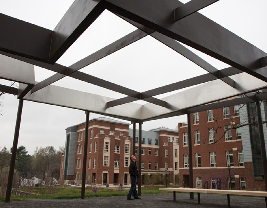 Image of a white man looking up at the steel-beam "Shadowcatcher" on the University of Virginia campus; brick buildings are seen in the background