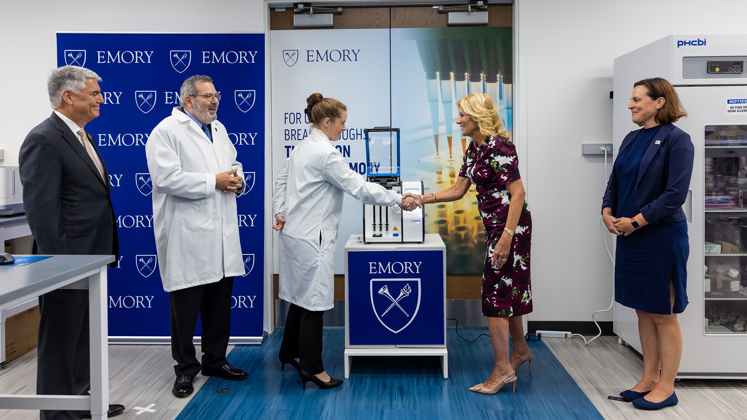 First lady Jill Biden shakes hands with a lab manager as Emory professor Phil Santangelo and President Gregory L. Fenves look on.
