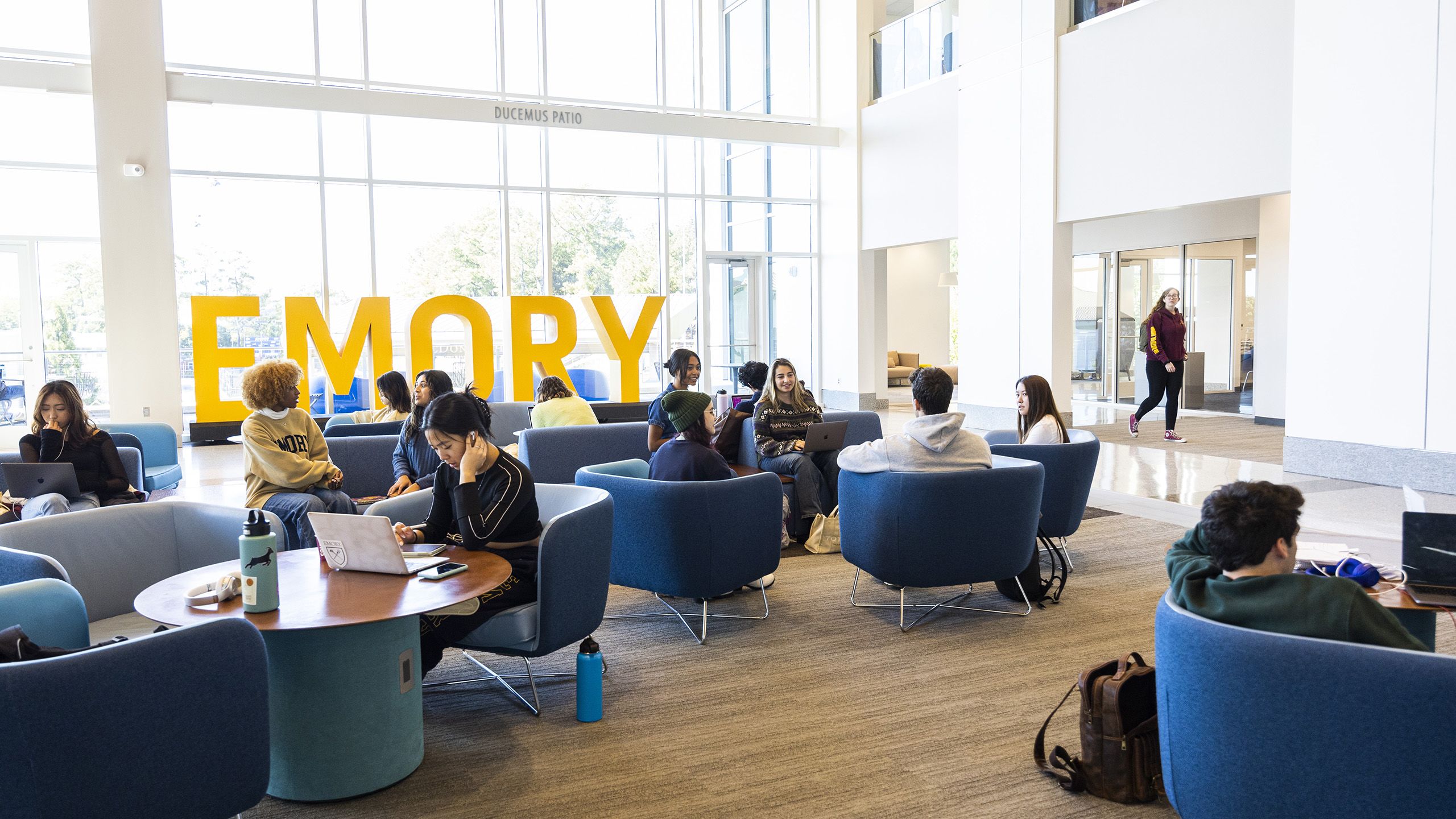 Group of Emory University students chatting and working on laptops in the Emory Student Center lobby