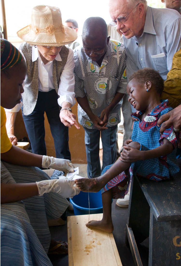 Adults gather round a crying child as an adult wearing rubber gloves tends to a wound in the child's foot.