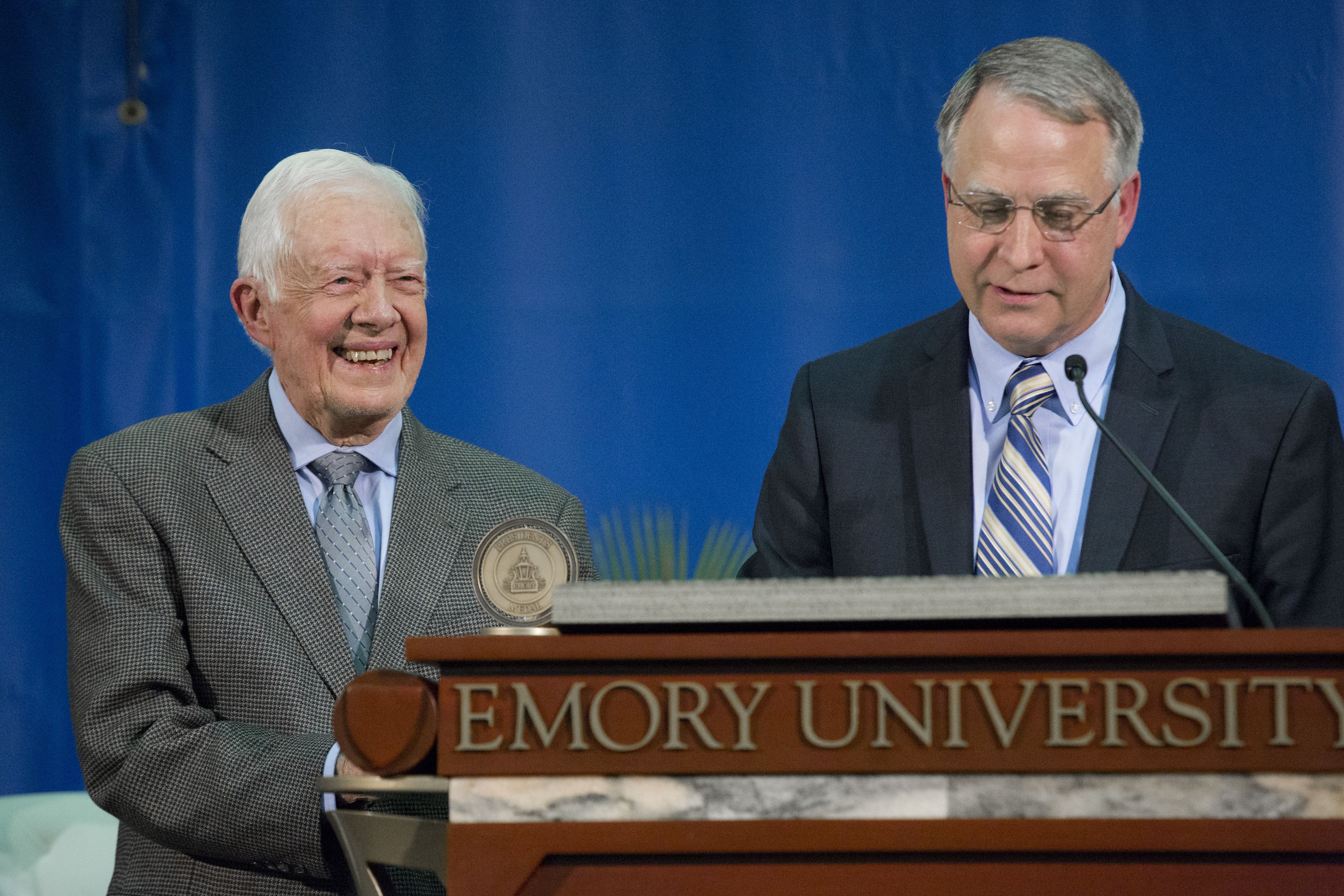 Carter, smiling next to a podium where Wagner is speaking.