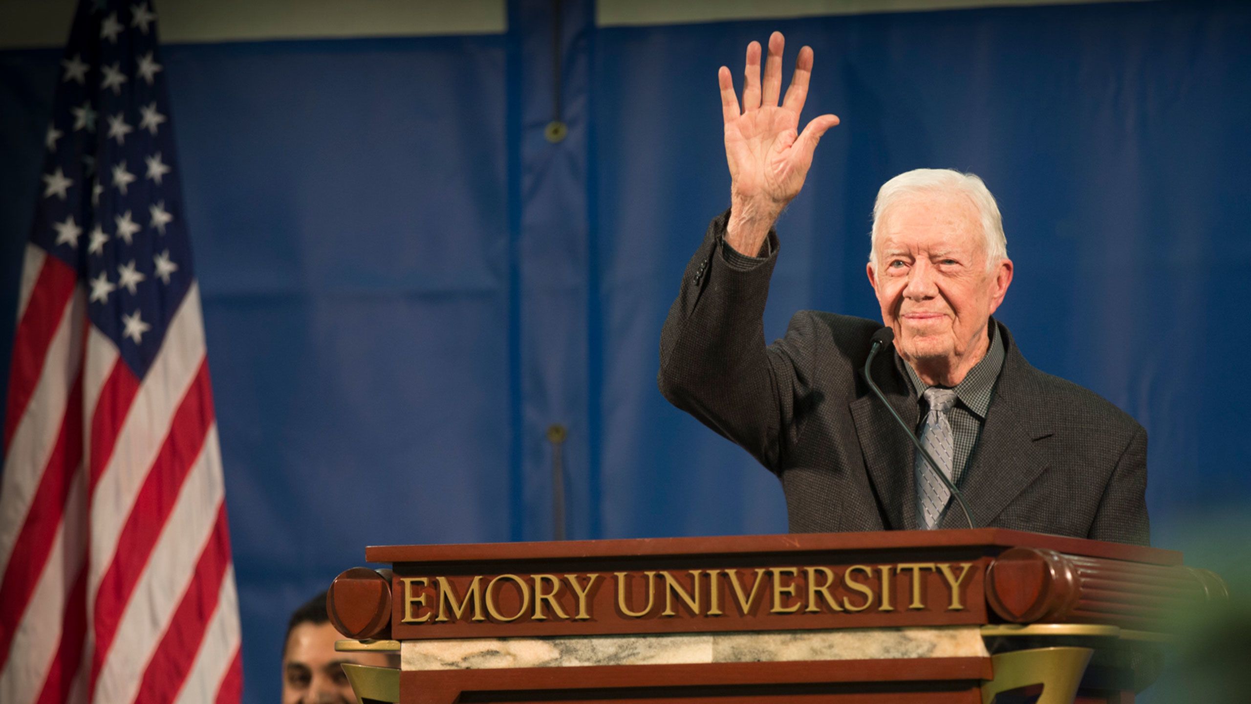 President Carter waves from an Emory podium with the American flag in the background