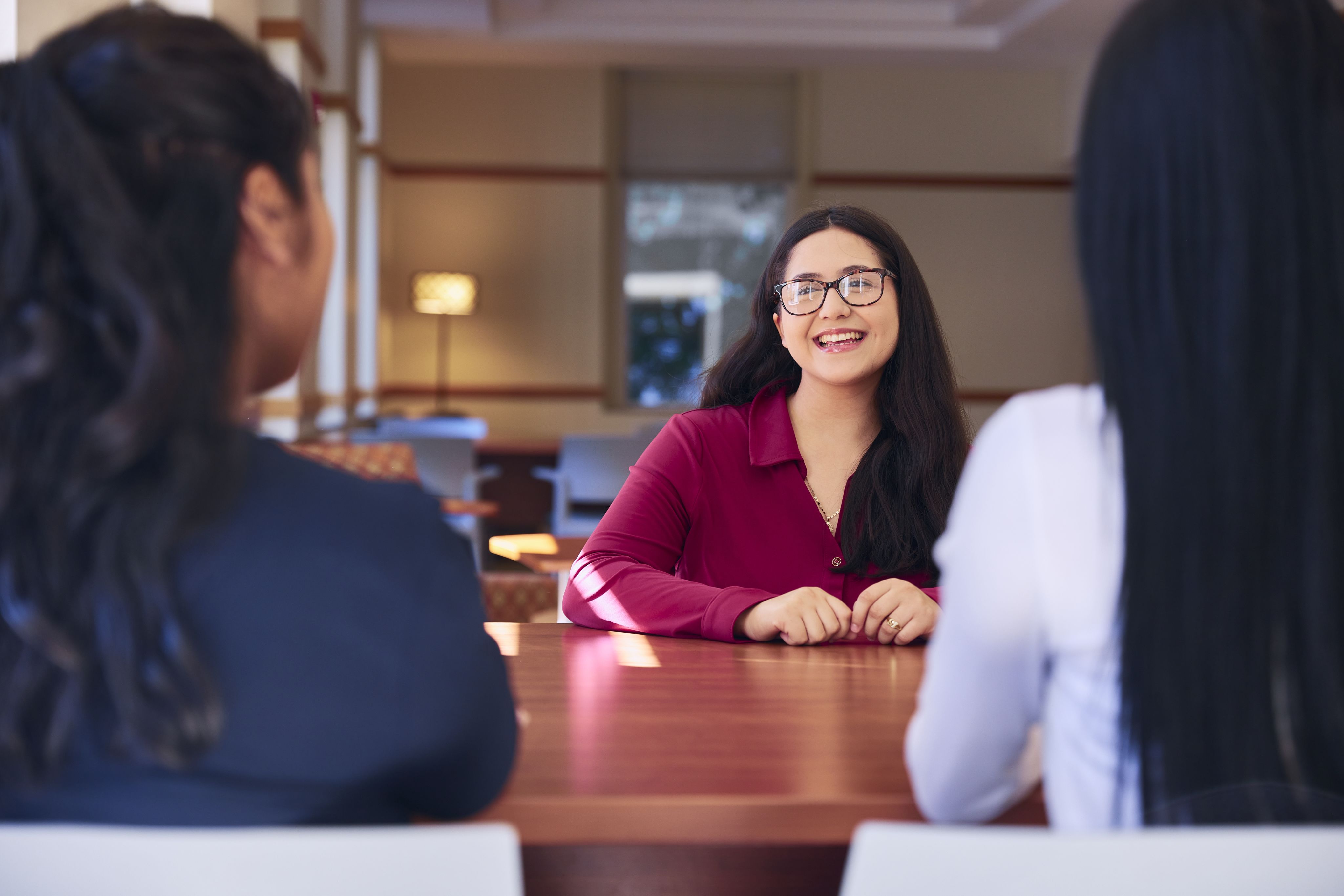 Student sitting at table facing two other students, smiling and having a conversation